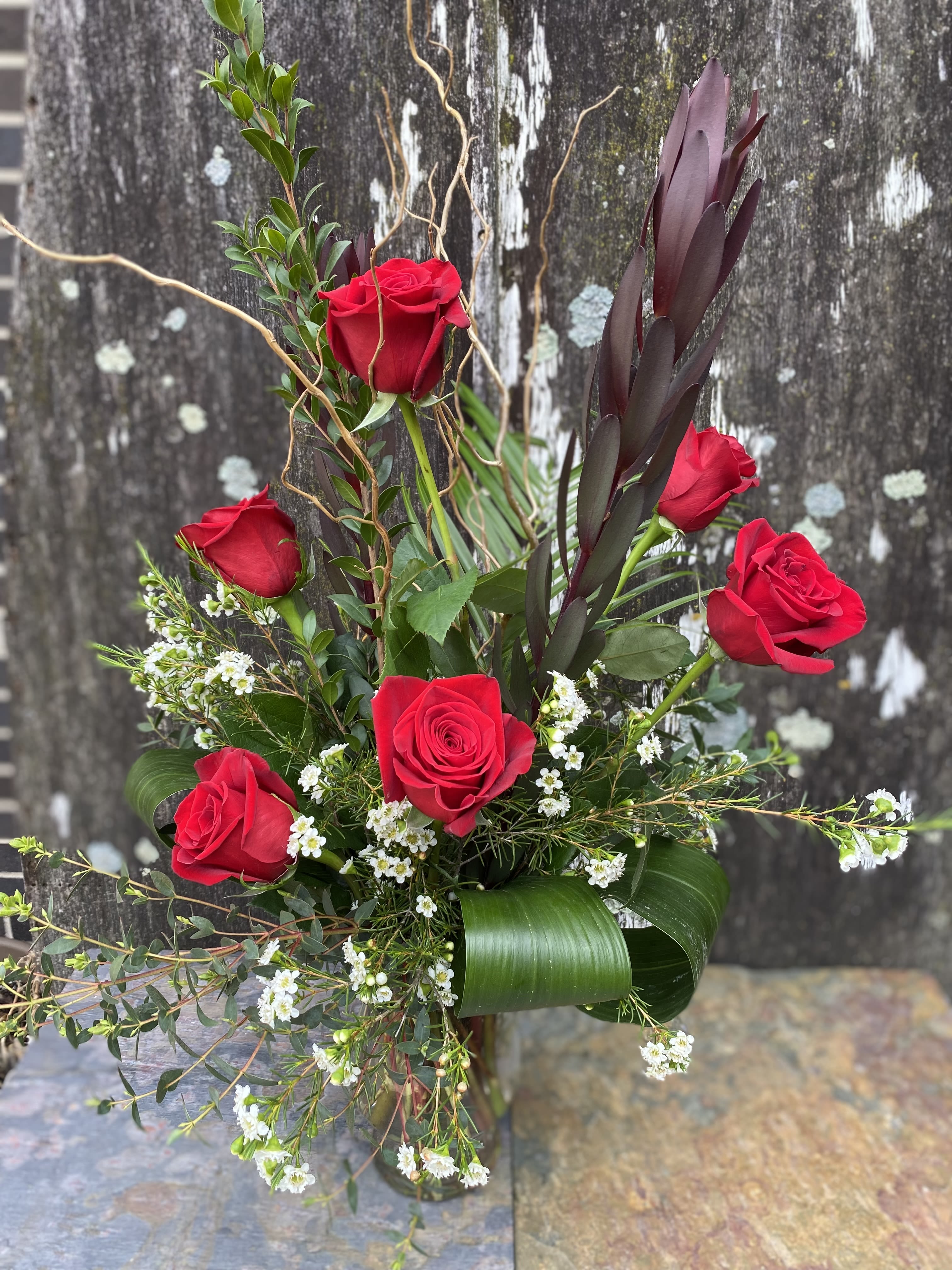 Red roses arranged with white filler flowers in a glass vase