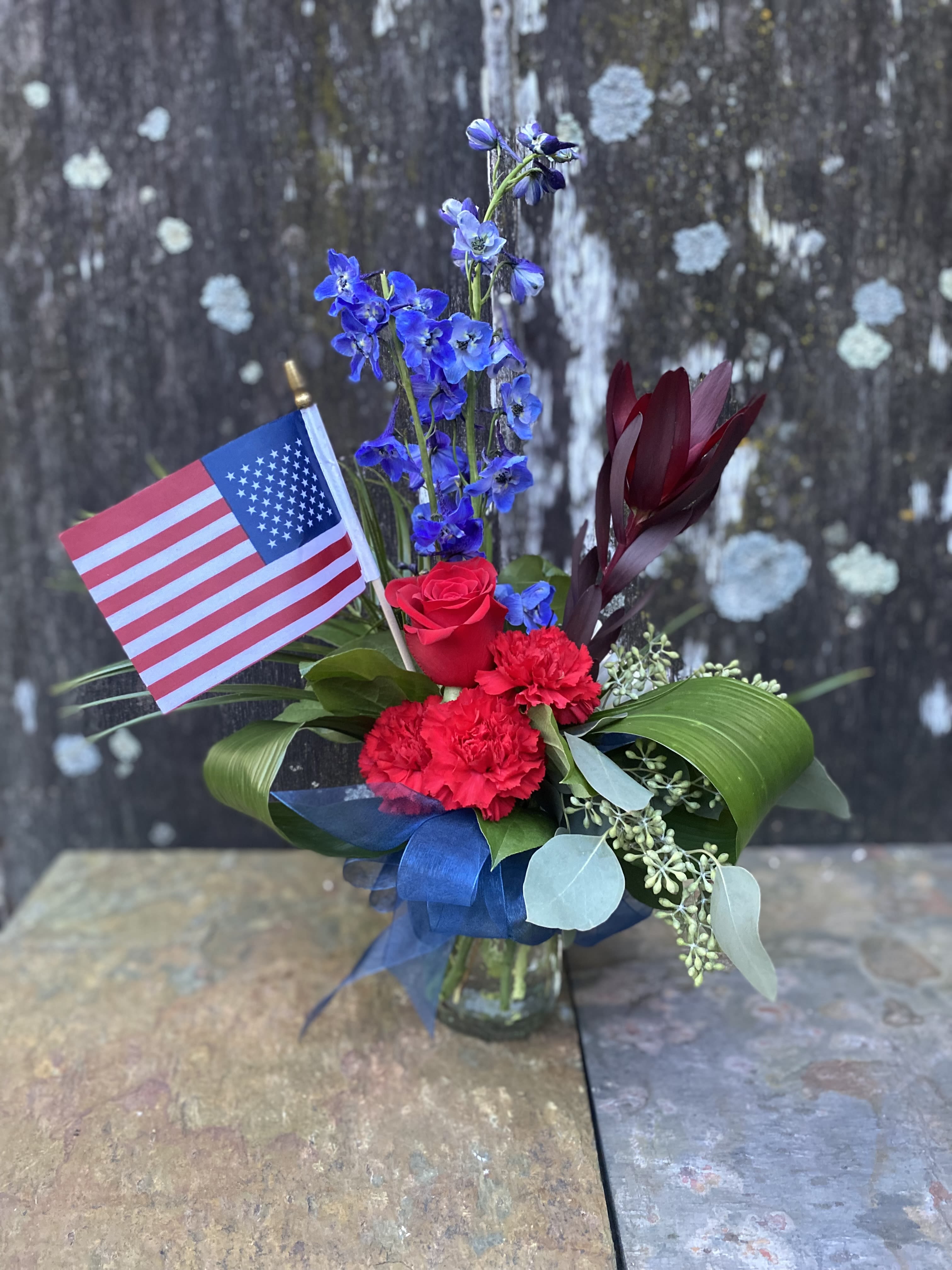 Red and blue floral arrangement in a glass vase with an American flag