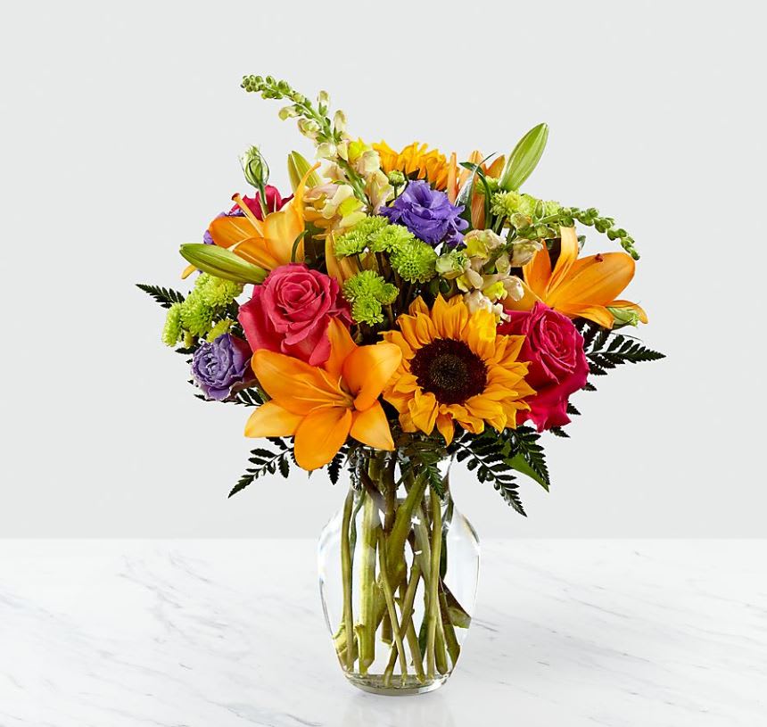 Best Day™ Bouquet- VASE INCLUDED - The Best Day™ Bouquet is ready to create a moment your recipient will always remember! An instant mood booster with it's mix of bright bold colors, this gorgeous fresh flower arrangement brings together sunflowers, hot pink roses, purple double lisianthus, orange LA Hybrid Lilies, yellow snapdragons, green button poms, and lush greens to make this day, their best day. Presented in a clear glass vase, this fresh flower arrangement is made just for you to help you send your warmest birthday, congratulations, or get well wishes to your favorite friends and family. GOOD bouquet is approx. 15"H x 12"W. BETTER bouquet is approx. 18"H x 13"W. BEST bouquet is approx. 18"H x 14"W. EXQUISITE bouquet is approx. 20"H x 15"W.  