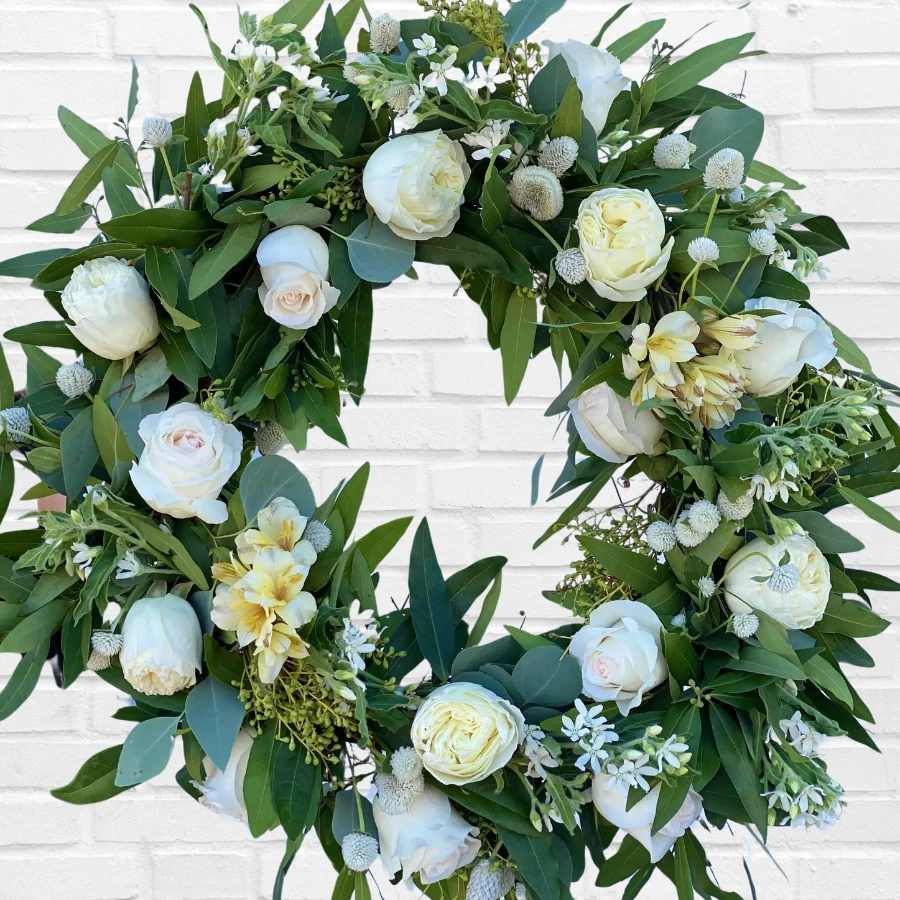 White floral wreath with roses and greenery on a white brick wall