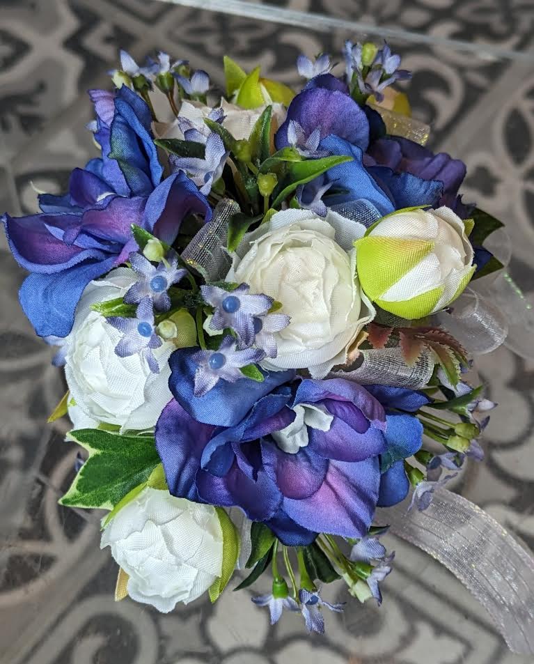 Blue Skies Silk Wrist Corsage - These are artificial flowers. The flowers and ribbon cannot be changed. It is currently on a white snap band but can be put on a black, silver or gold snap band if needed, if they are available.