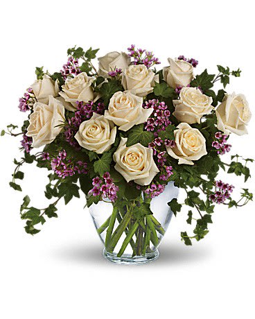 Cream roses in a clear glass vase with purple filler flowers