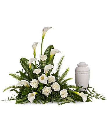 White funeral floral arrangement with calla lilies and roses beside an urn