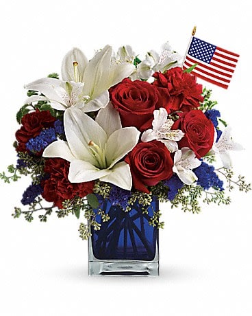 Red roses and white lilies in a blue glass vase with a small American flag