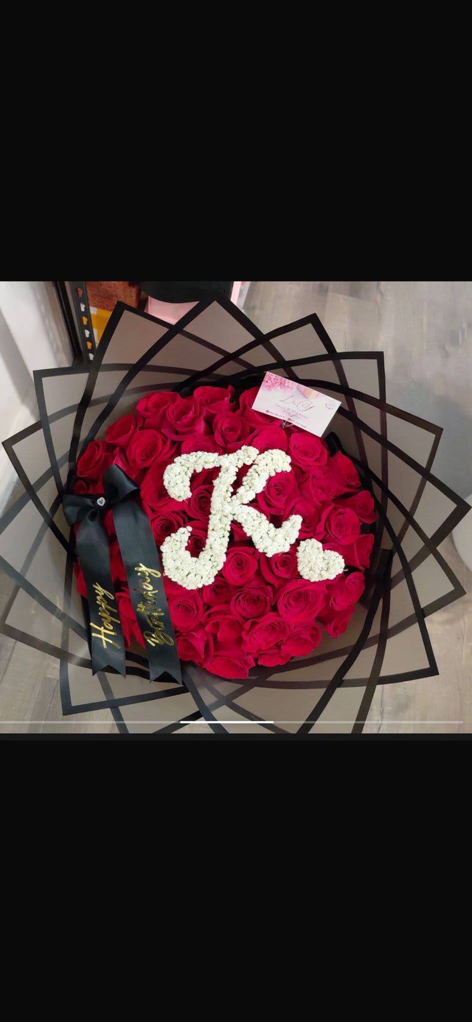 Iniciales de Amor Purpura - Bouquet compuesto por 50 rosas rojas premium, diseñado con elegantes capas de papel negro y detalles personalizados con iniciales en baby breath.