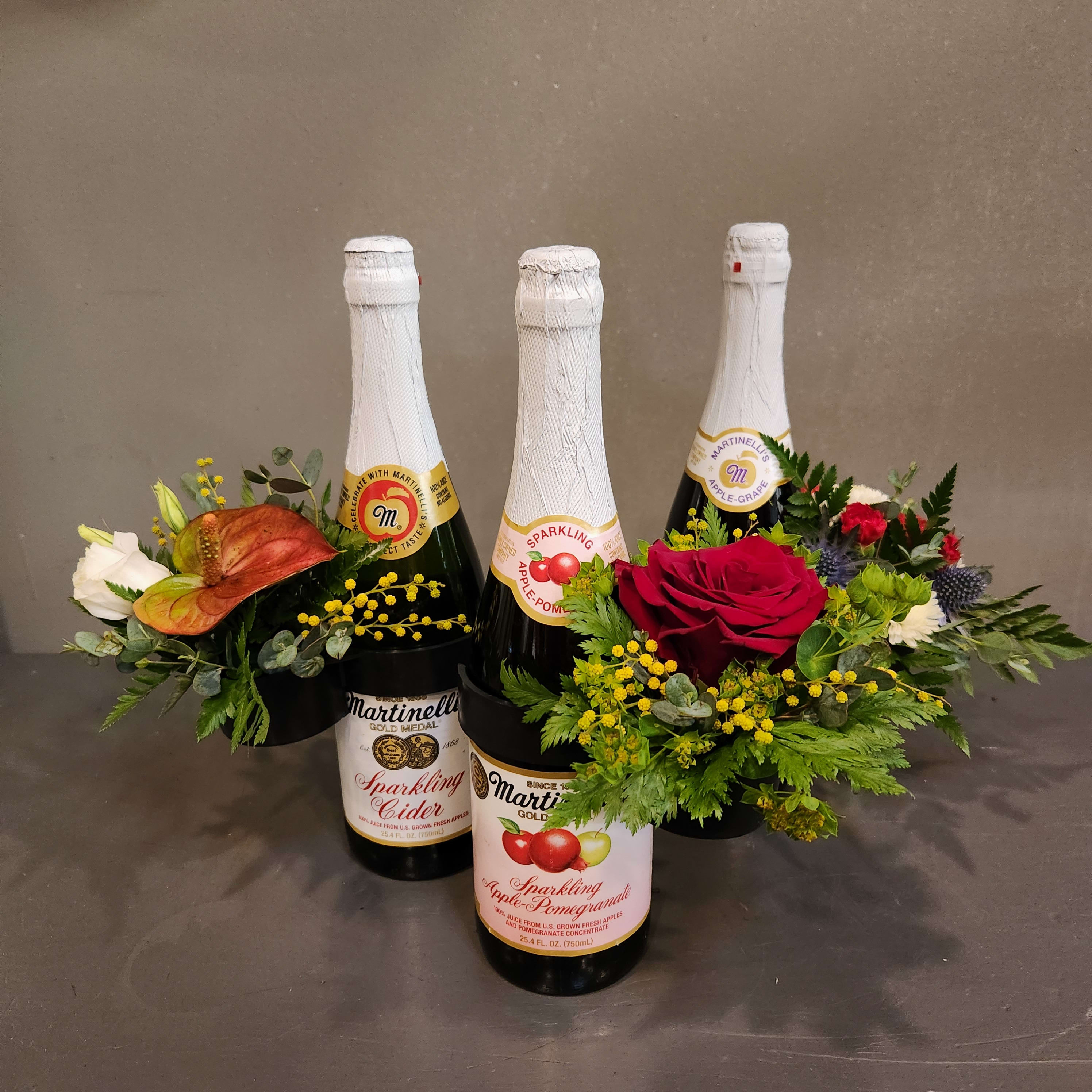 Three sparkling cider bottles arranged with flowers and greenery