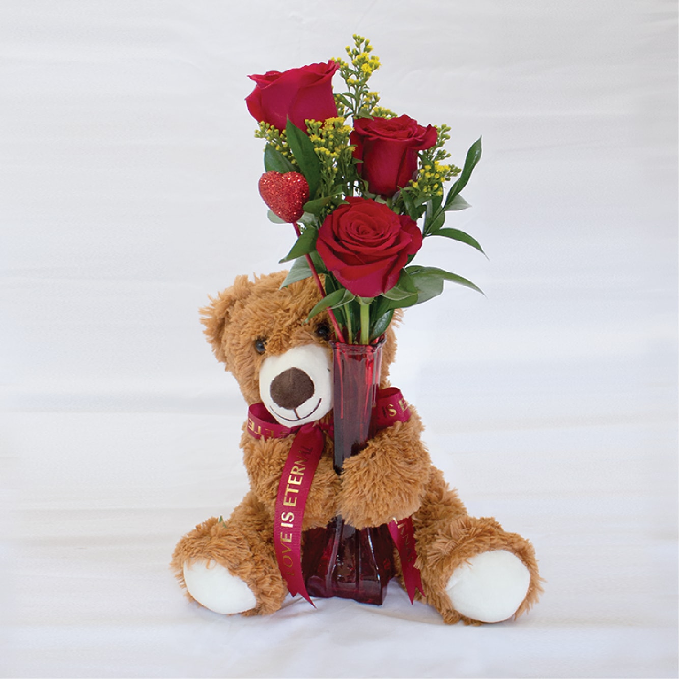 Teddy bear holding a vase of red roses with a heart pick