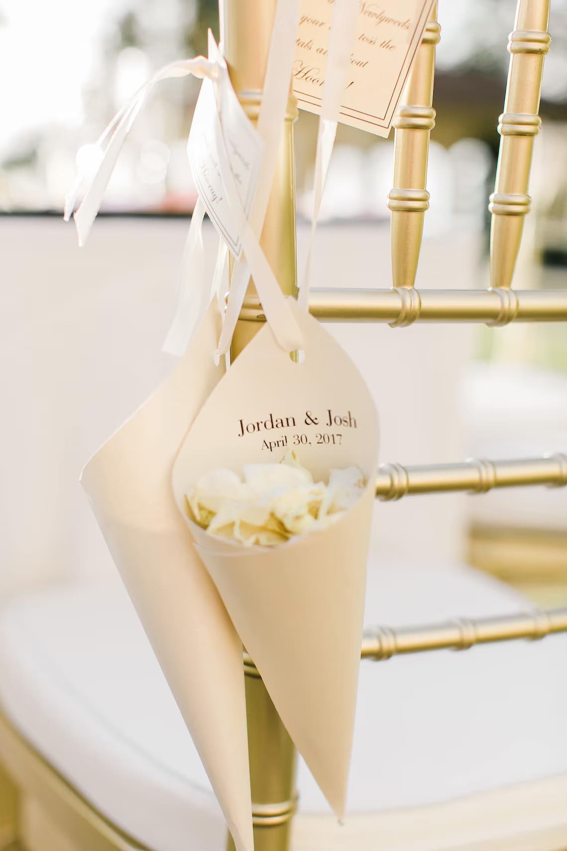 Cream wedding favor cones tied to a gold chair with white ribbon