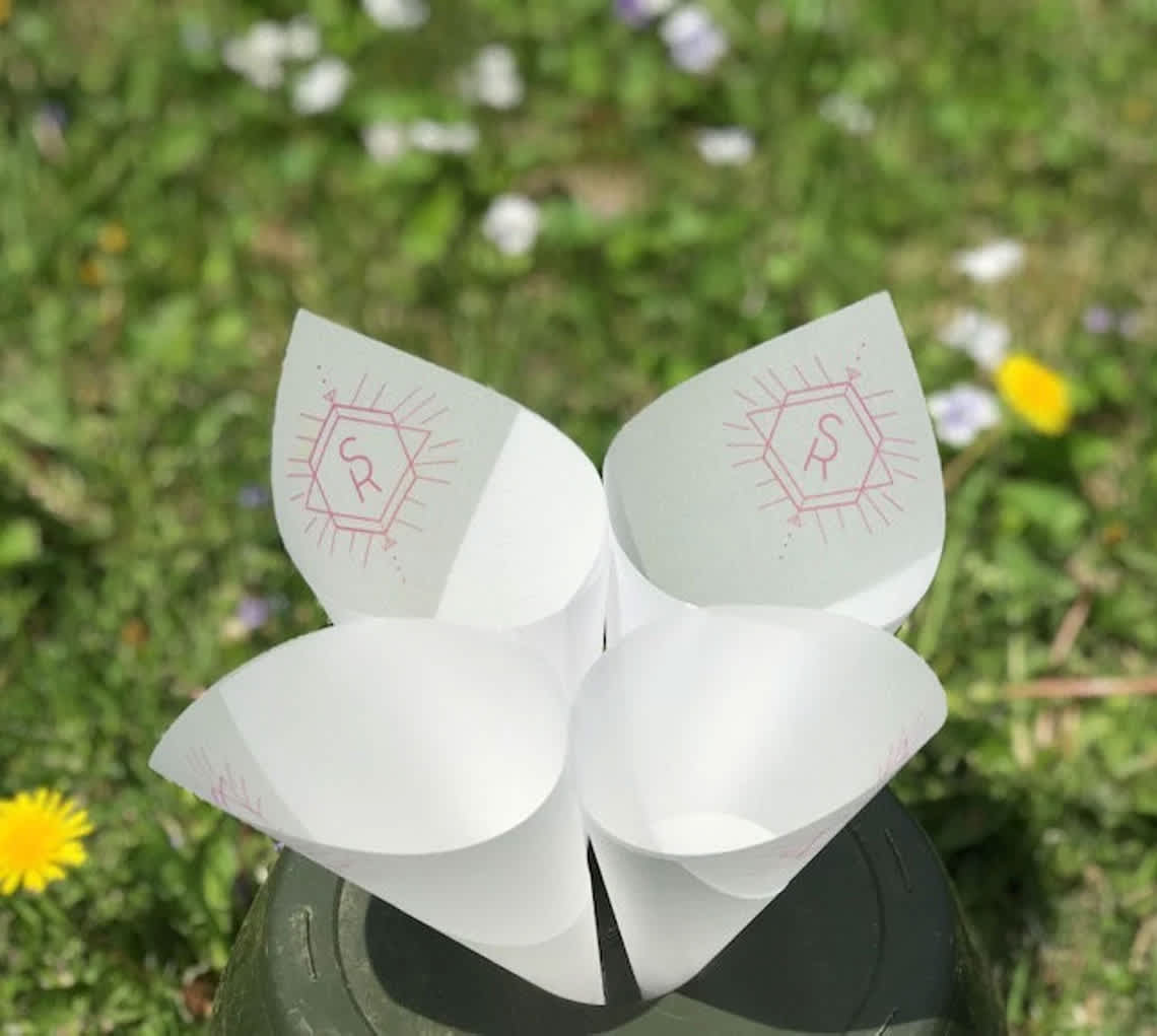 Four white paper cone holders with pink monogram marks on a dark base