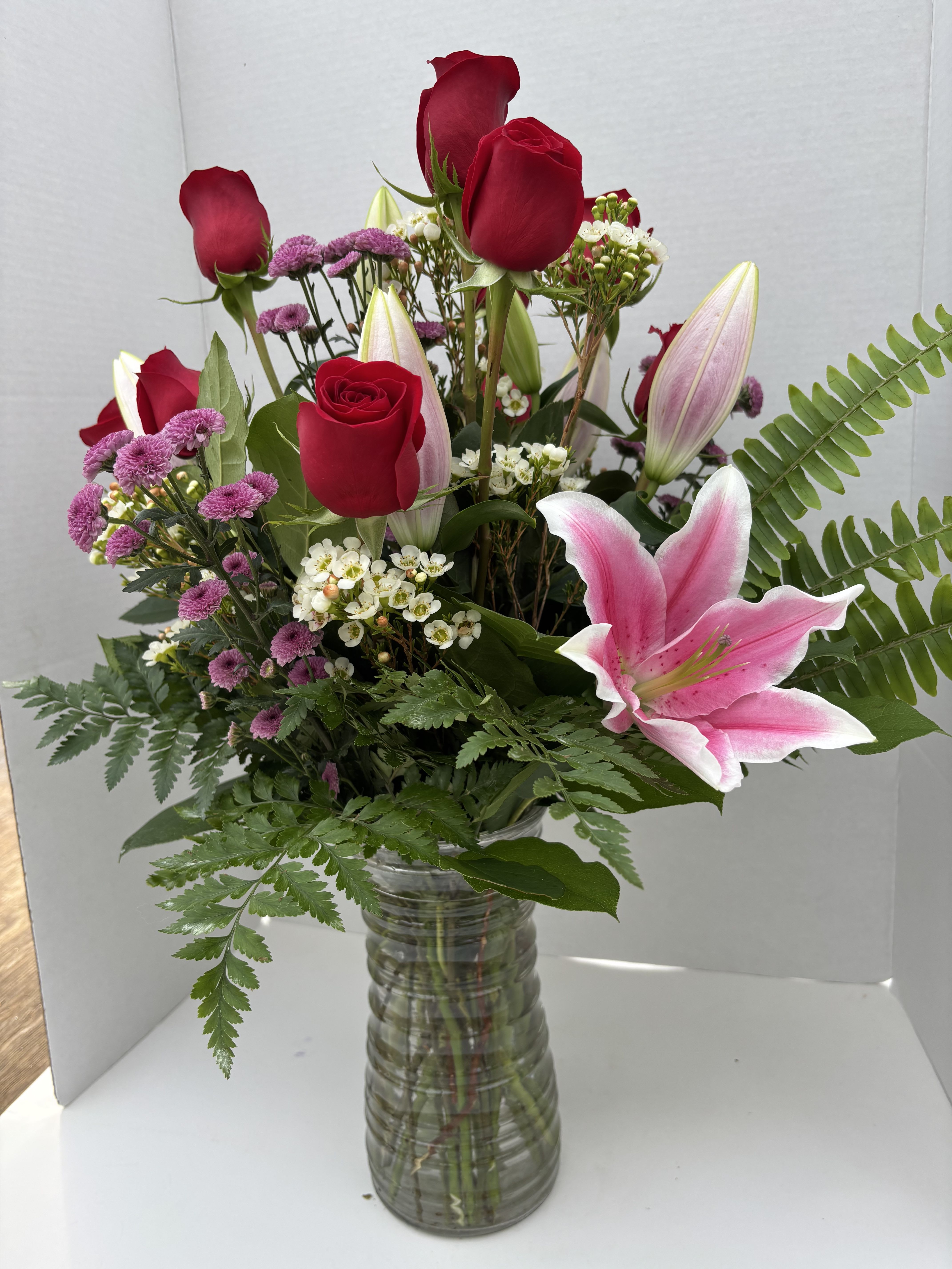 Mixed bouquet of red roses, pink lilies, and purple flowers in a glass vase