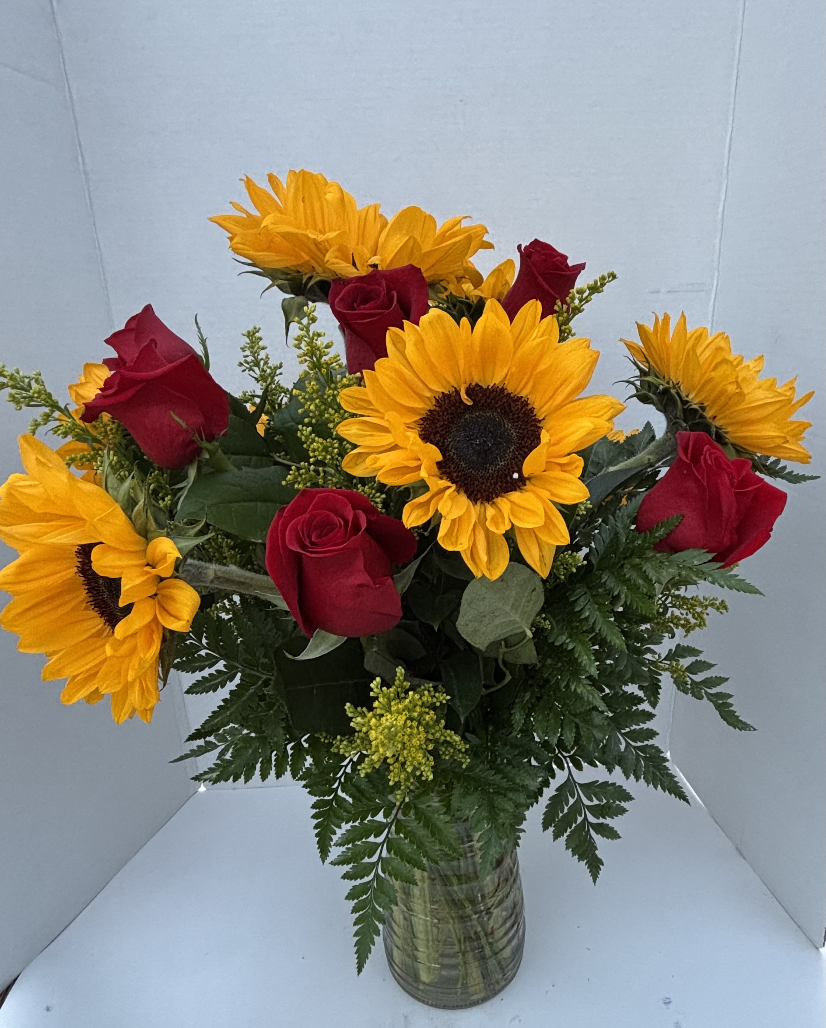 Bouquet of red roses and yellow sunflowers in a glass vase