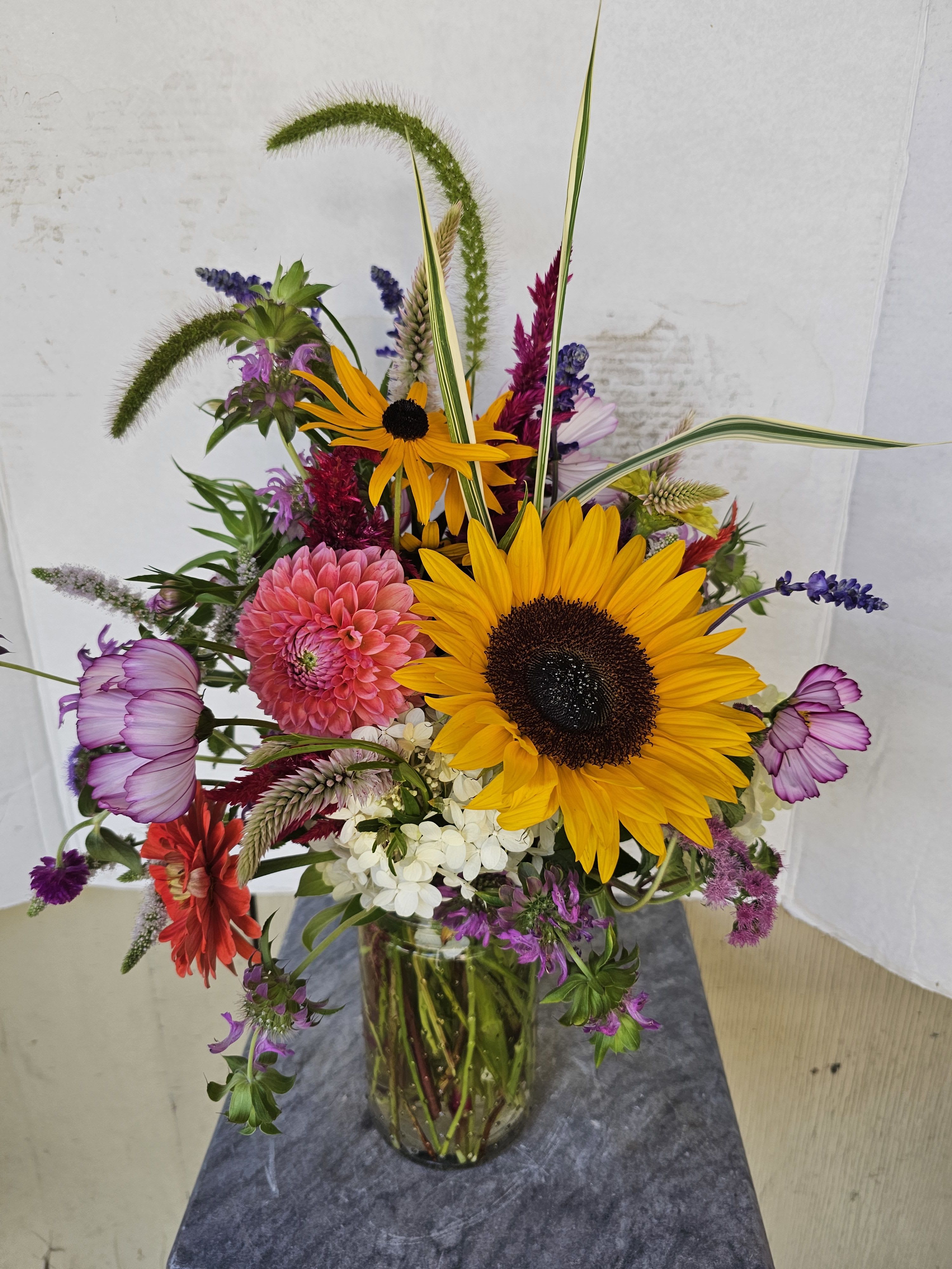 Mixed bouquet with sunflowers, pink blooms, and purple flowers in a glass vase