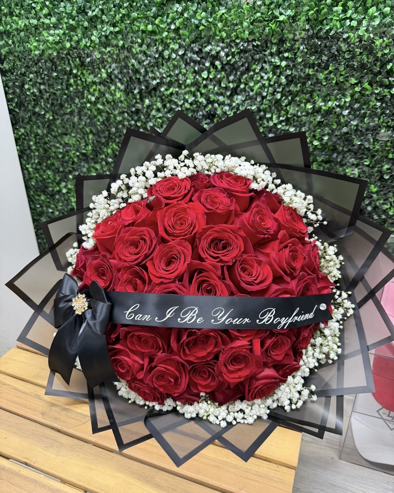 Round bouquet of red roses with white baby's breath and a black ribbon.