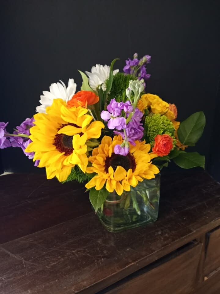 Mixed bouquet with sunflowers, daisies, and purple flowers in a glass vase