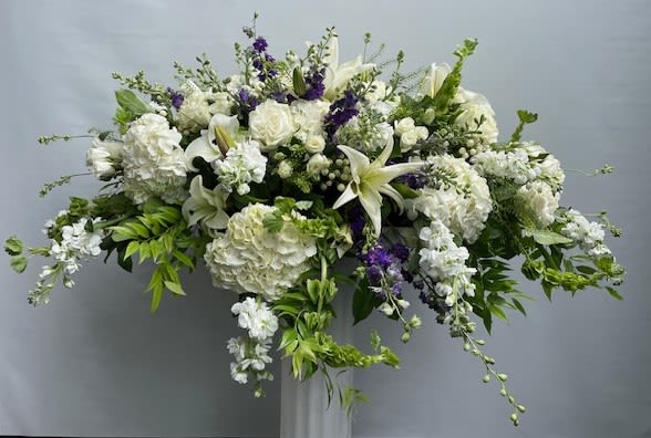 Large white floral arrangement with lilies and roses on a pedestal