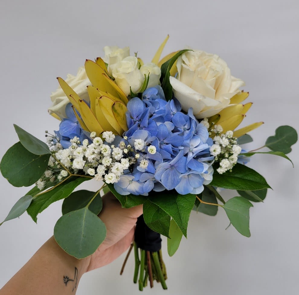 Nosegay in Cool Color Tone - Celebrate life’s most cherished moments with our Nosegay in Cool Color Palette, a hand-held bouquet that combines elegance and versatility. Featuring a lush base of hydrangeas, complemented by roses, tiny spray roses, and natural greenery, this arrangement is perfect for proms, homecoming dances, recitals, weddings, and more. Its timeless design and serene color palette make it a standout accessory for any special occasion. **Key Features:  *Hydrangeas: Known for their voluminous blooms and soft hues, hydrangeas add texture and elegance to the bouquet. They are a favorite for weddings and formal events due to their versatility and charm. *Roses and Spray Roses: Classic roses and delicate spray roses bring a romantic and sophisticated touch, perfectly complementing the hydrangeas. *Natural Greenery: Eucalyptus, ivy, or other greenery adds depth and freshness, creating a multidimensional and organic feel. *Hand-Tied Design: A compact, easy-to-carry arrangement that exudes timeless beauty and grace. **Benefits: *Perfect for formal events, adding elegance and sophistication to your ensemble. *Customizable to match your event’s theme or color palette. *Handcrafted with care to ensure freshness and quality. Order this nosegay today to add a touch of cool-toned sophistication to your special day!