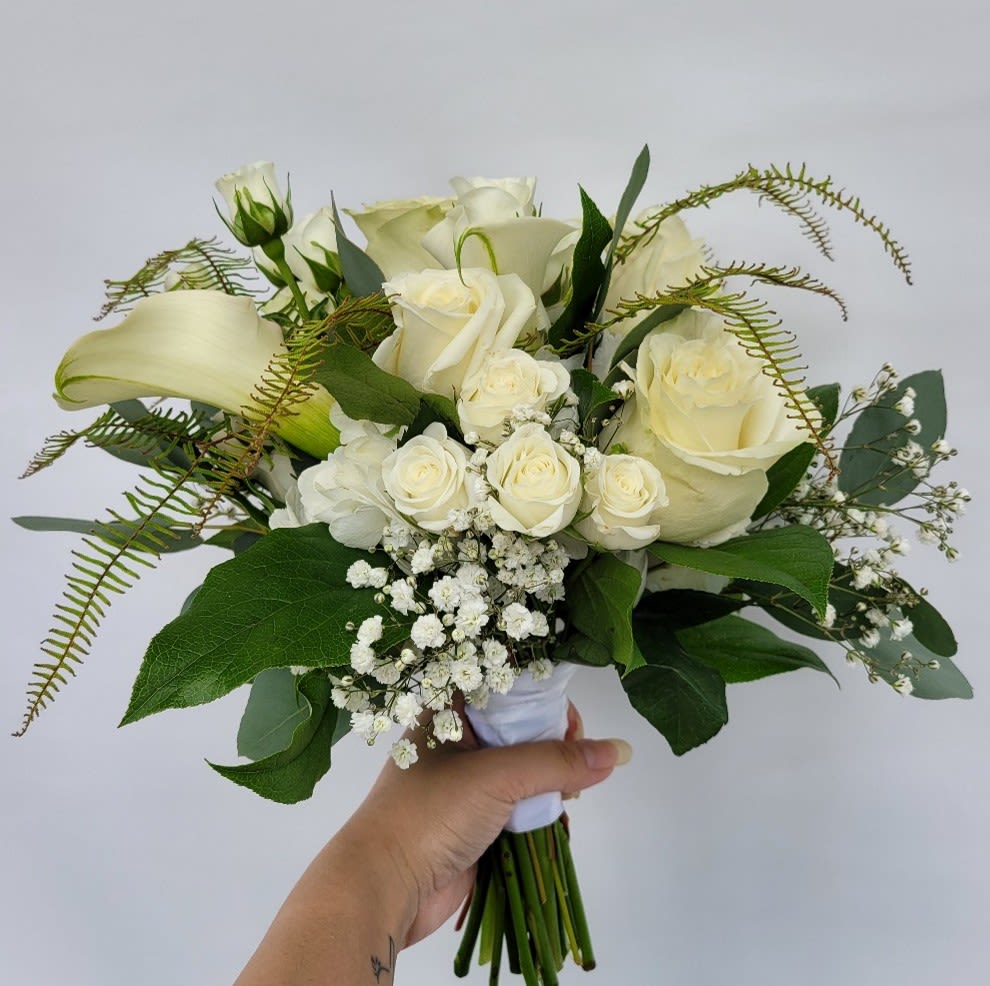 Nosegay in Neural Color Palette - Elevate your special moments with our Nosegay in Neutral Color Palette, a hand-held bouquet that exudes timeless elegance. Featuring a harmonious blend of white hydrangeas, roses, tiny spray roses, and natural greenery, this arrangement is designed to complement life’s most cherished occasions. Perfect for proms, homecoming dances, recitals, and weddings, its serene whites and greens create a sophisticated and graceful aesthetic. The shown version includes the addition of calla lilies for an extra touch of refinement. Benefits: Perfect for formal occasions, adding a touch of sophistication to your ensemble. Neutral tones ensure versatility, complementing any outfit or event theme. Handcrafted with care to ensure freshness and quality. This nosegay is a celebration of understated beauty, combining lush textures and serene tones to create a bouquet that’s both timeless and versatile. Order today to make your special day unforgettable!