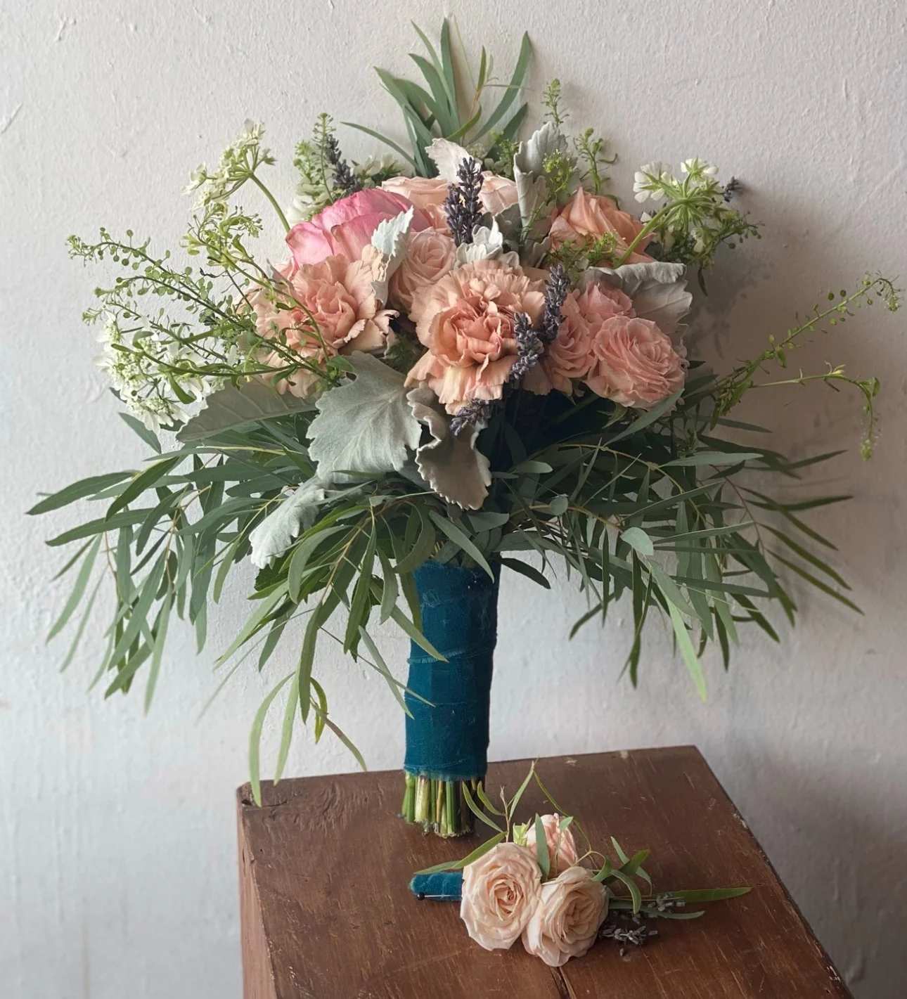Blush rose bouquet with greenery and a matching boutonniere on a table