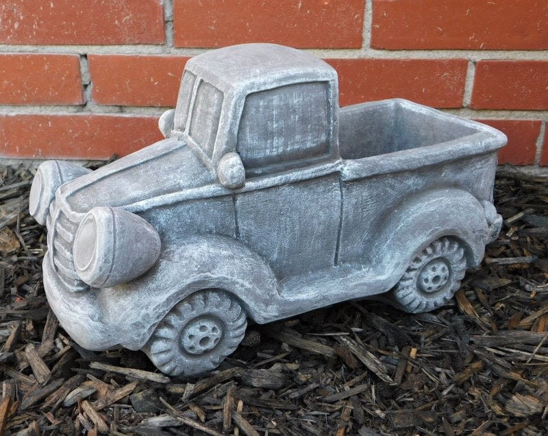 Gray pickup truck-shaped planter on mulch in front of a brick wall