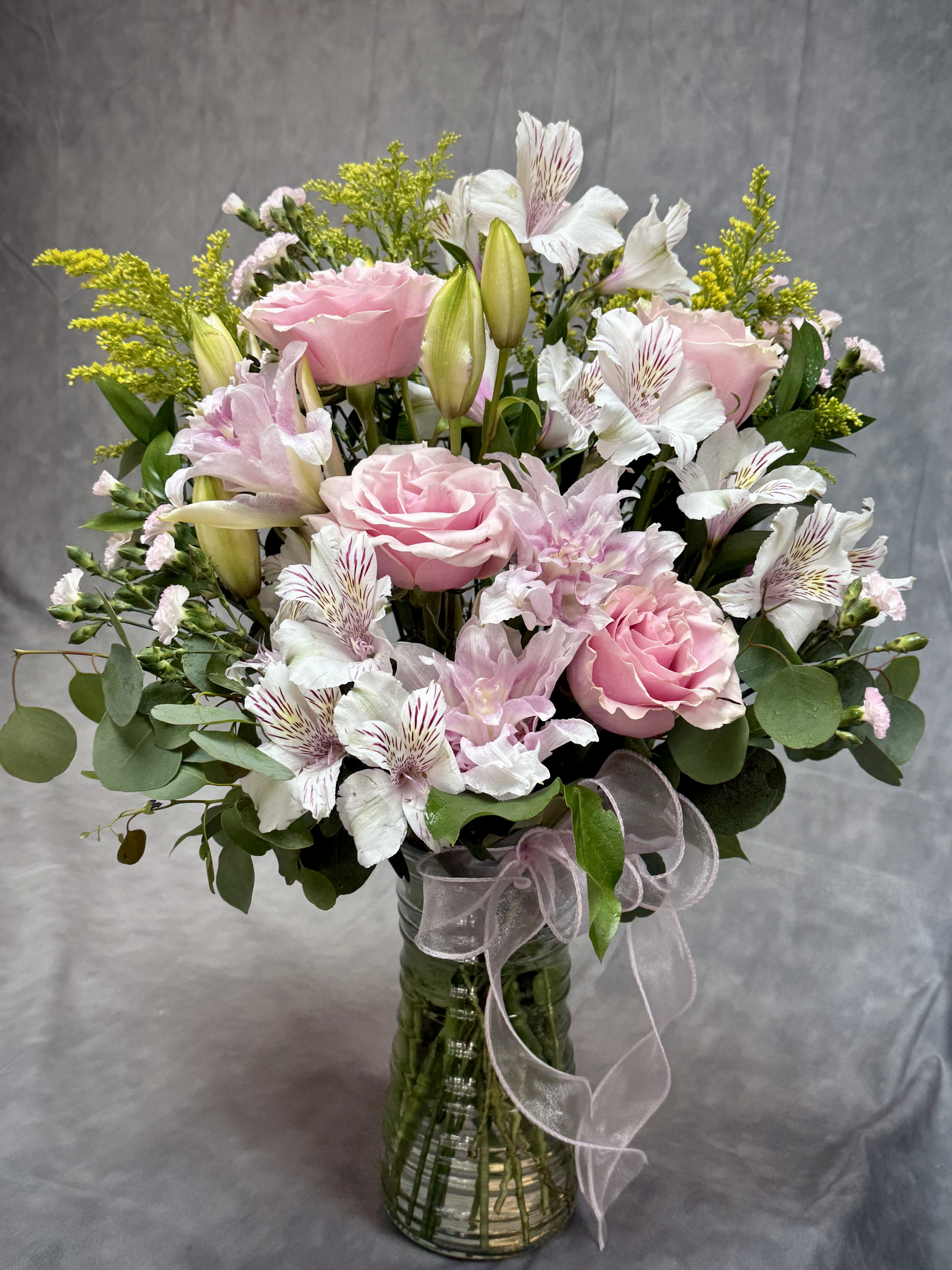 Pink roses and white lilies in a glass vase with a ribbon