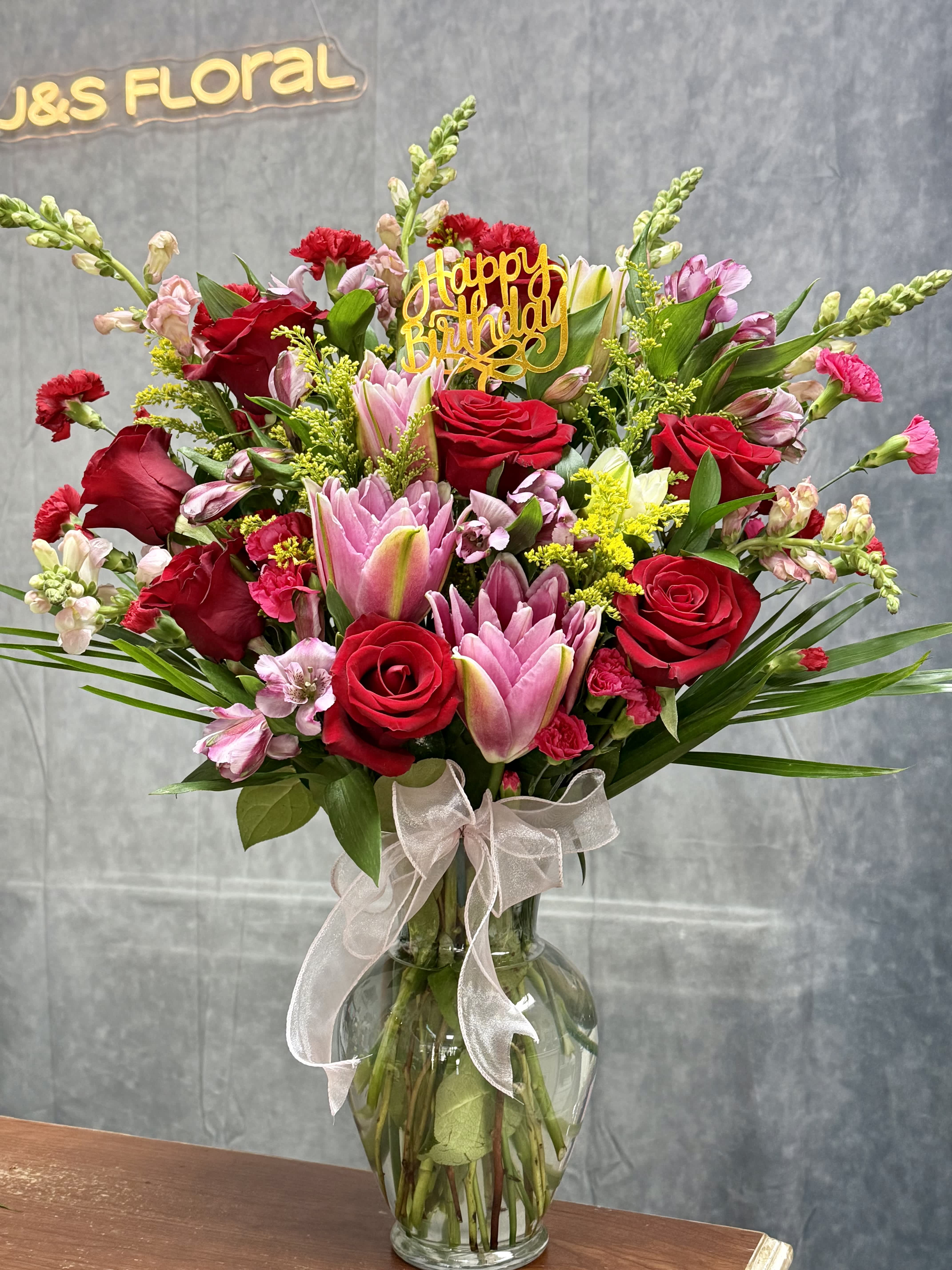 Bouquet of red roses and pink lilies in a glass vase with a birthday topper