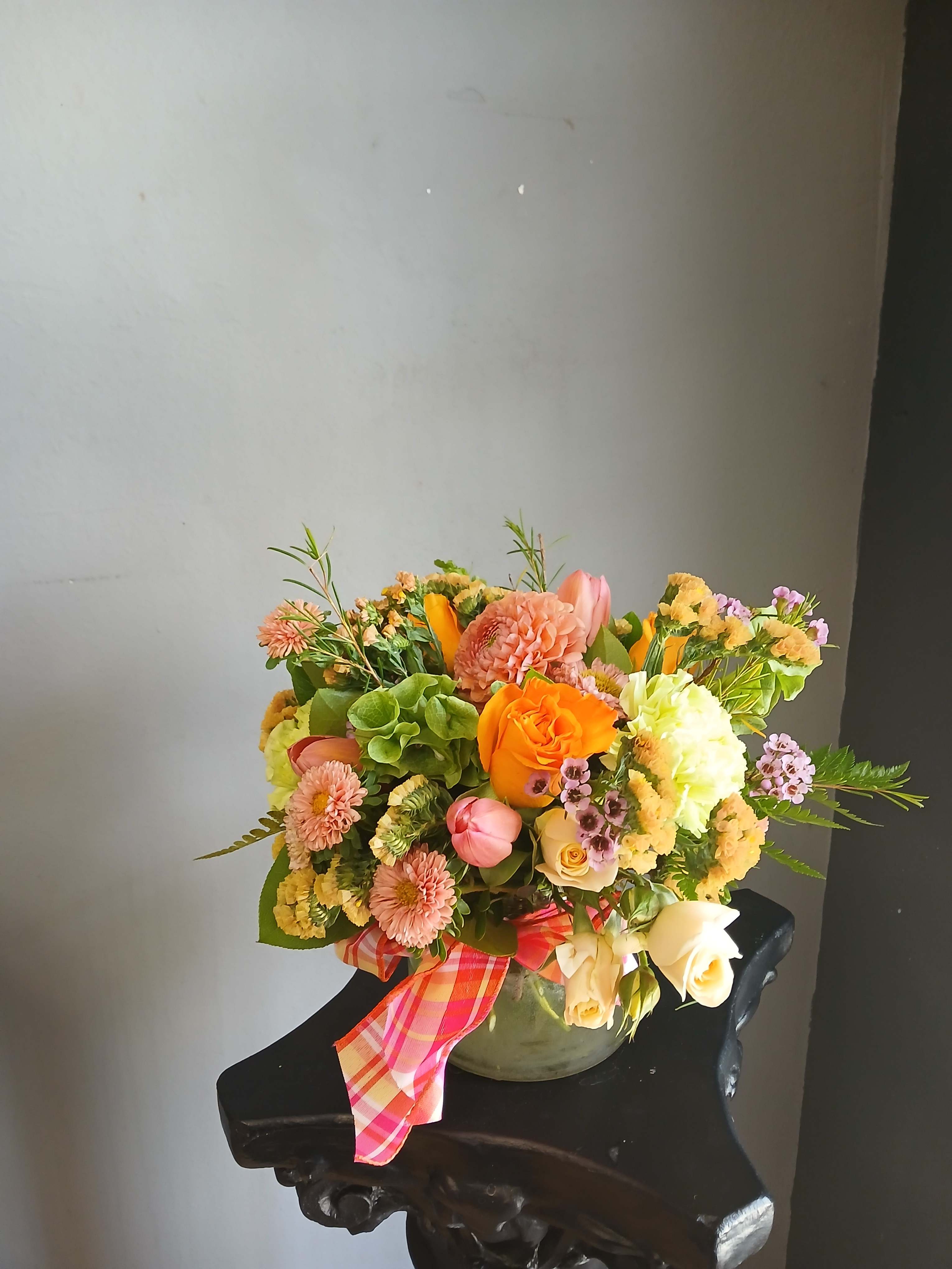 Mixed bouquet of orange, pink, and cream flowers in a vase with a plaid ribbon