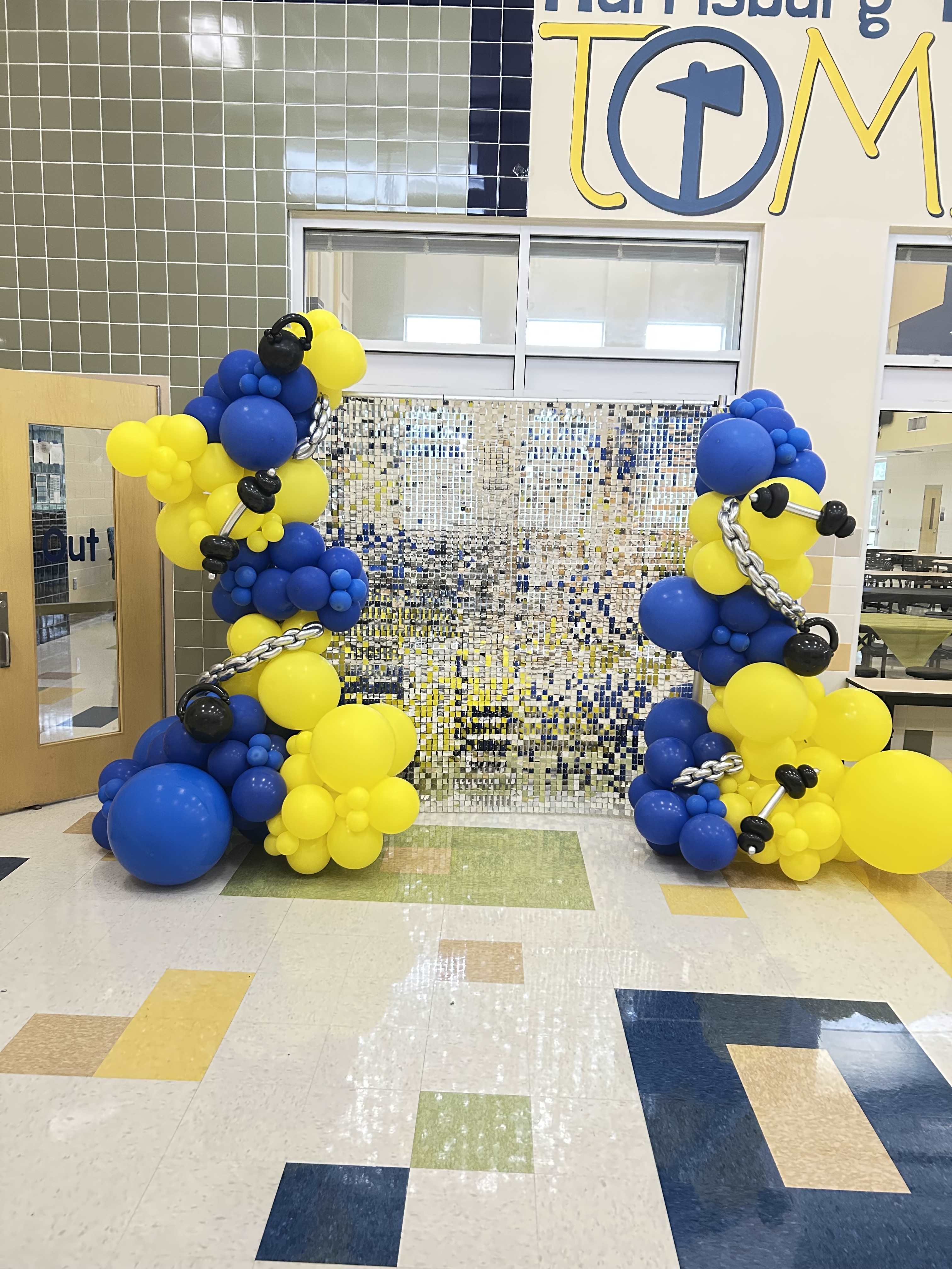 Blue and yellow balloon columns with black accents in a school hallway