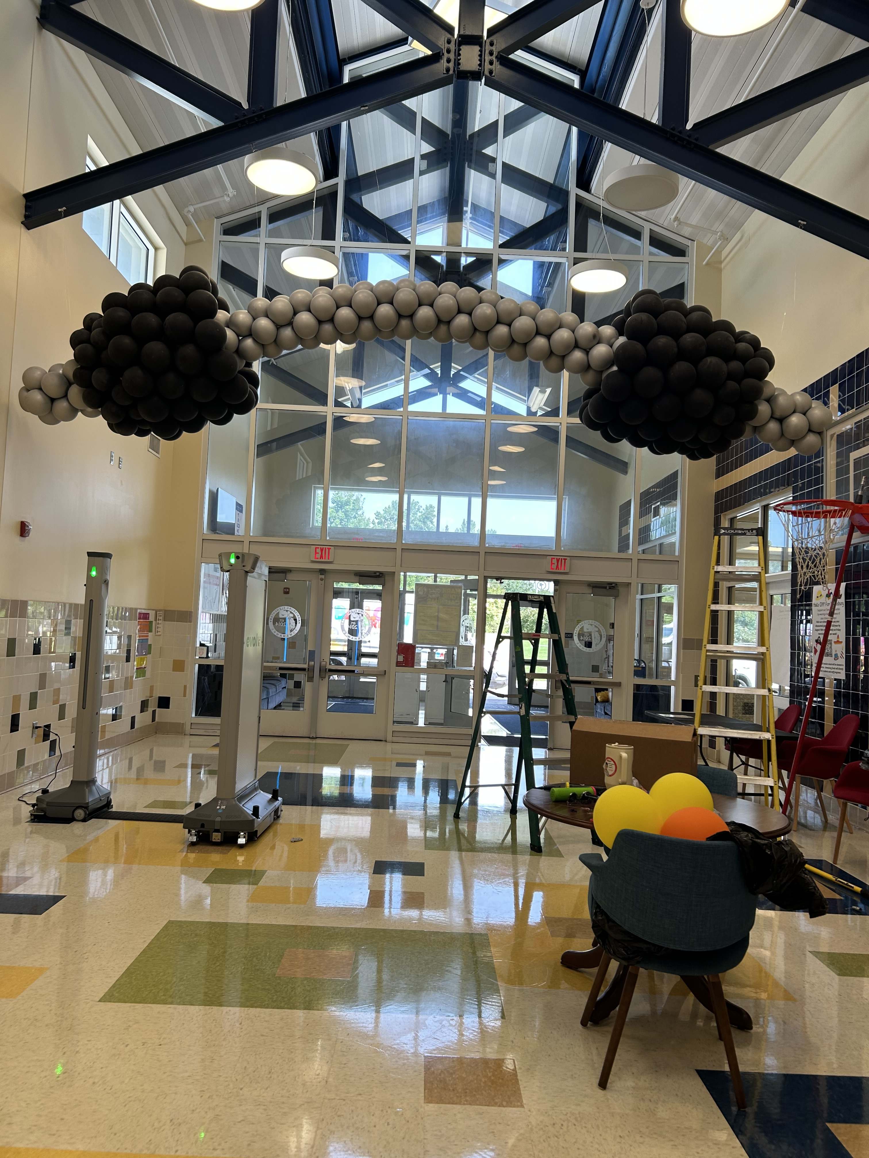 Black and gray balloon arch in a lobby with ladders and chairs