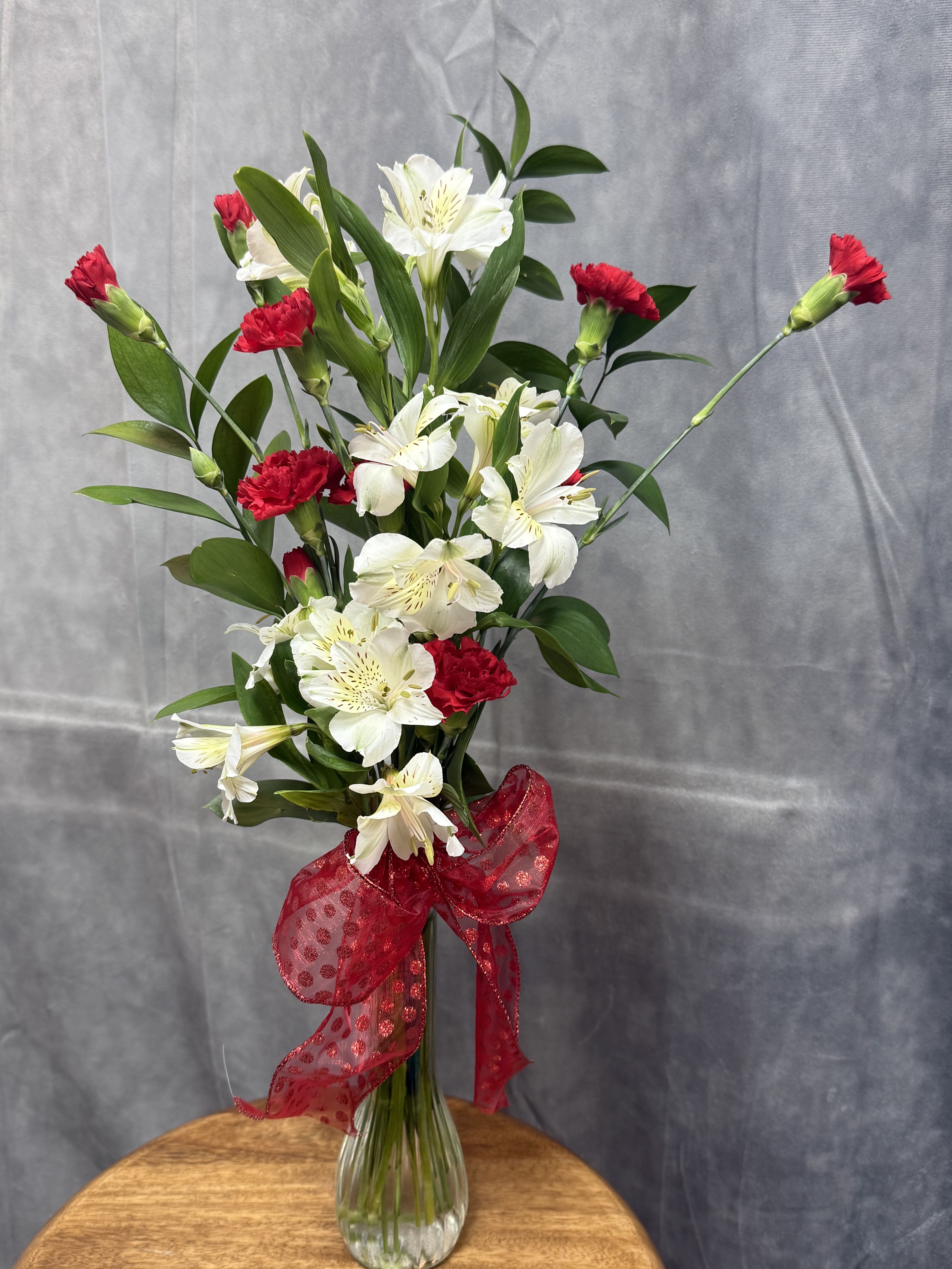 White alstroemeria and red carnations in a clear glass vase with a red bow.