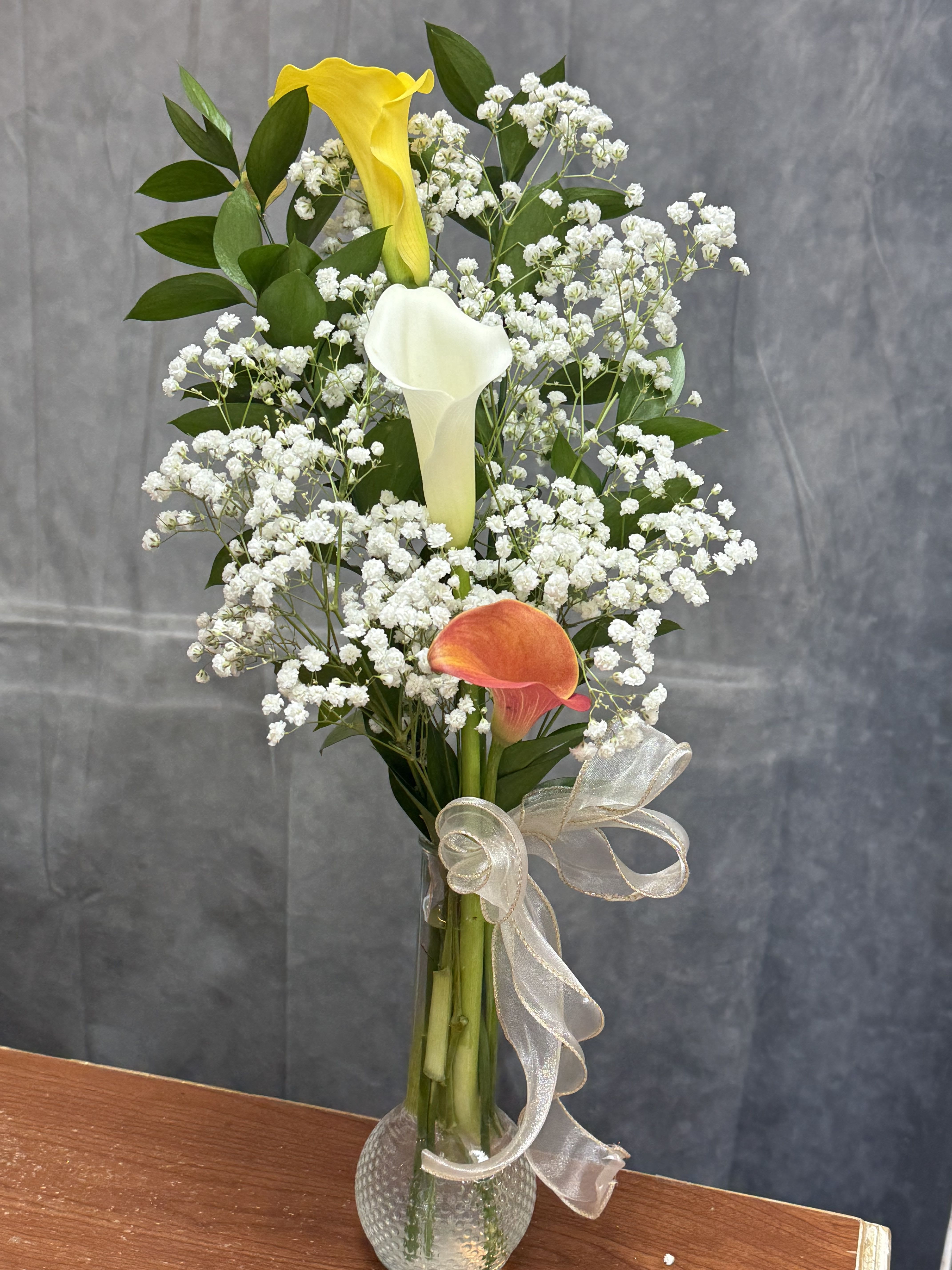Mix Calla Lily Bud Vase - Elegant and timeless, this charming vase arrangement features a beautiful mix of calla lilies accented with delicate baby’s breath and fresh greenery. Designed in a clear glass vase and finished with a graceful ribbon, it makes a perfect gift for birthdays, thank yous, sympathy, or simply brightening someone’s day with beauty and elegance. 