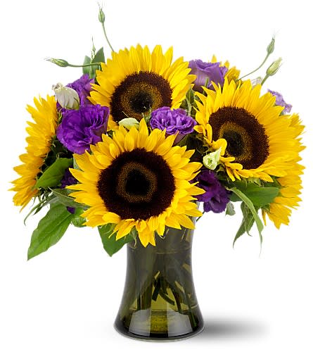 Teleflora's Smile Awhile - The rustic charm of sunflowers combined with the royal elegance of lisianthus. A disarmingly different floral arrangement that's sure to make any hostess bloom.    A light green glass silo vase, overflowing with six large sunflowers, set off with three stems of purple lisianthus, accented with assorted greens.    Approximately 15" (W) x 16" (H)    Orientation: All-Around    As Shown : TF-WEB12