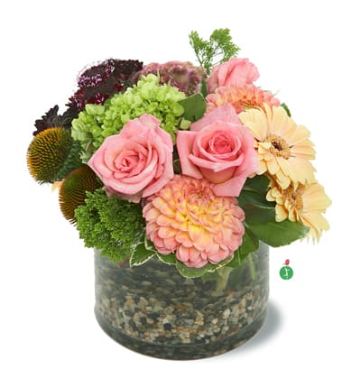 Pink roses and mixed blooms arranged in a glass vase with pebbles
