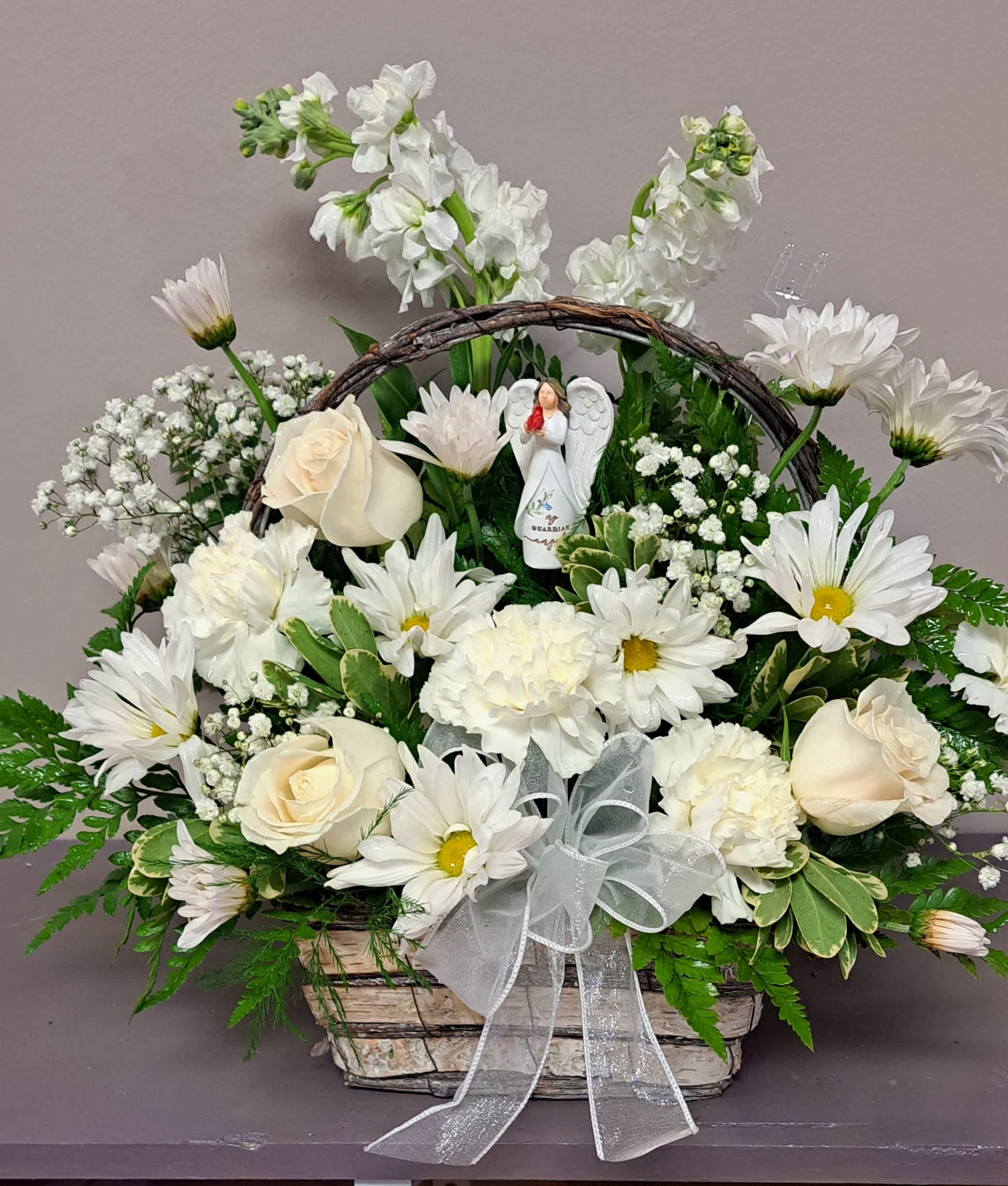 White flowers arranged in a basket with a ribbon and angel figurine