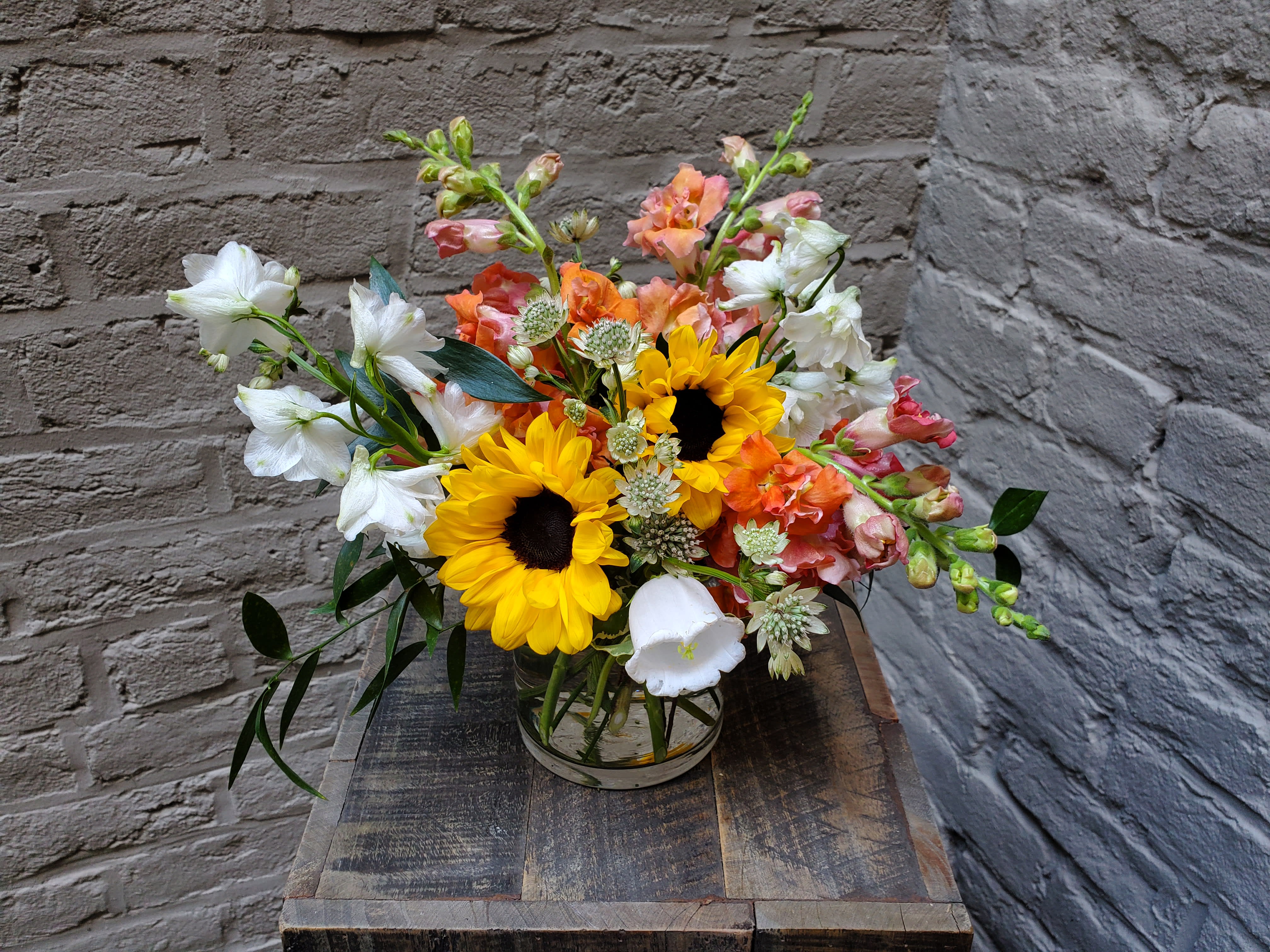 Mixed bouquet with sunflowers, white blooms, and orange flowers in a glass vase