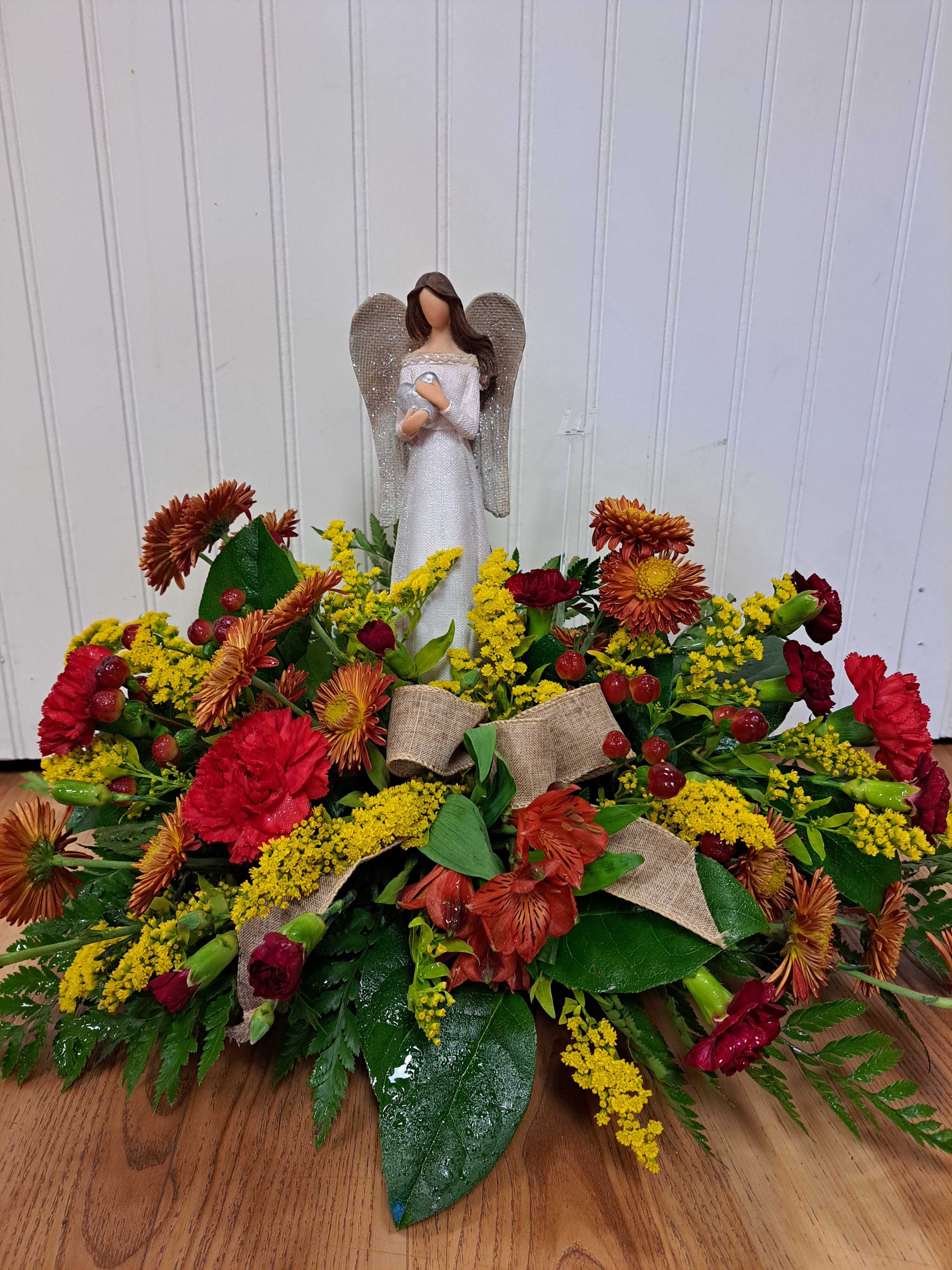 Angel figurine above a low floral arrangement with red and yellow blooms