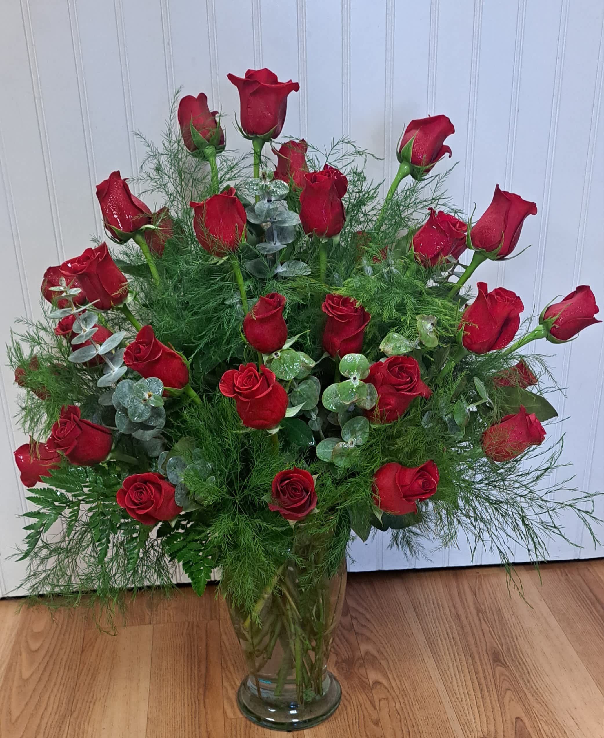 Red roses arranged in a clear glass vase with airy greenery