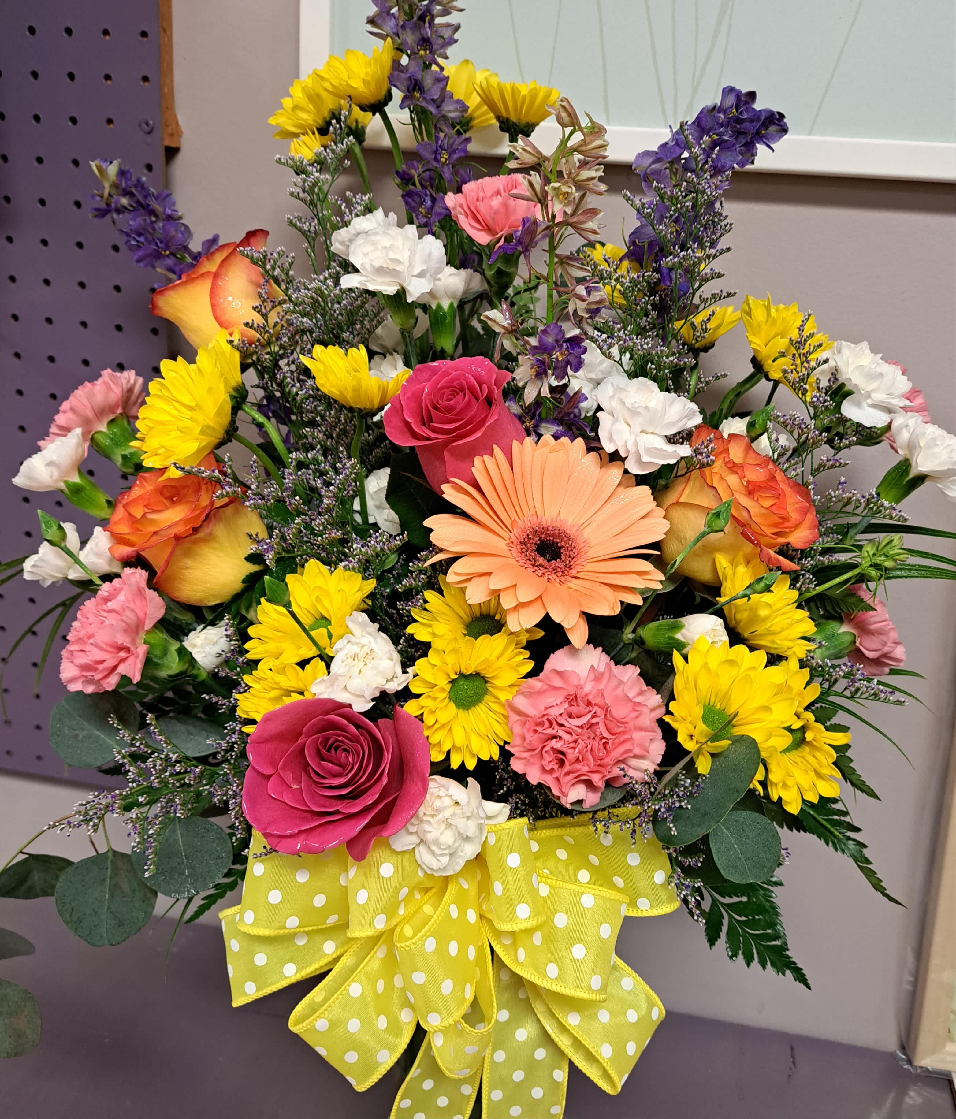 Colorful mixed bouquet with roses, daisies, carnations, and a yellow polka-dot ribbon