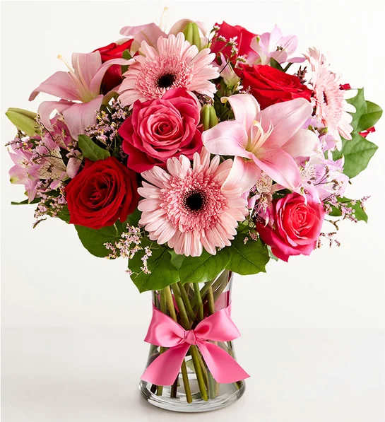Bouquet of pink lilies, red roses, and pink gerbera daisies in a glass vase