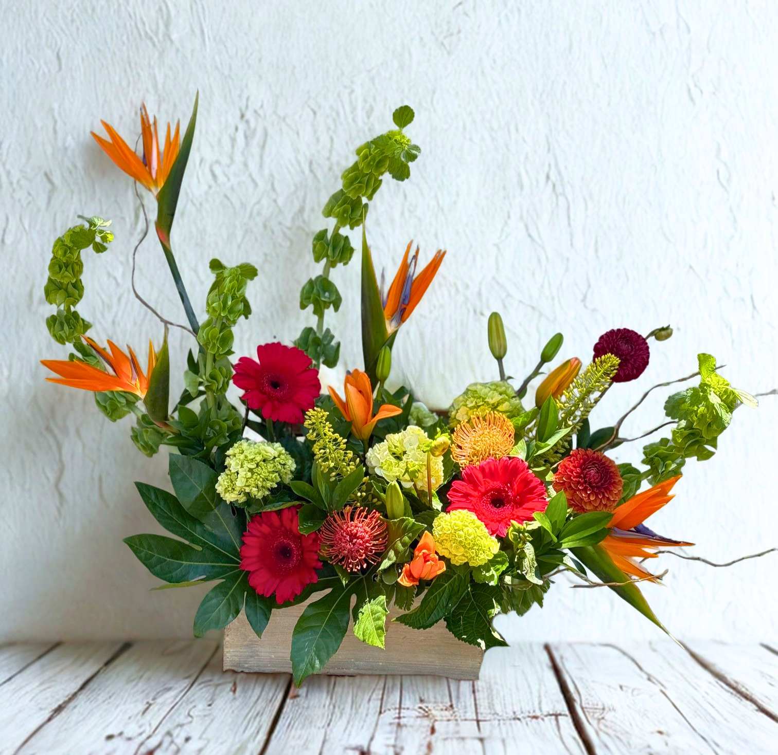 Mixed floral arrangement with orange bird-of-paradise and pink gerbera daisies in a wooden box