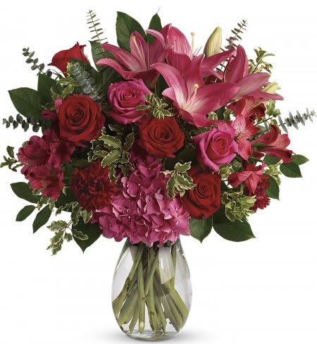 Arrangement of red and pink roses, lilies, carnations, and hydrangeas in a clear glass vase