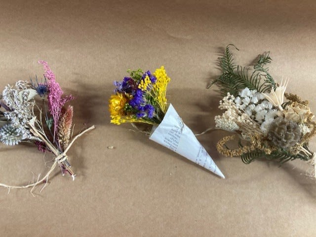 Three small dried flower bouquets on brown paper, including purple, yellow, and white arrangements