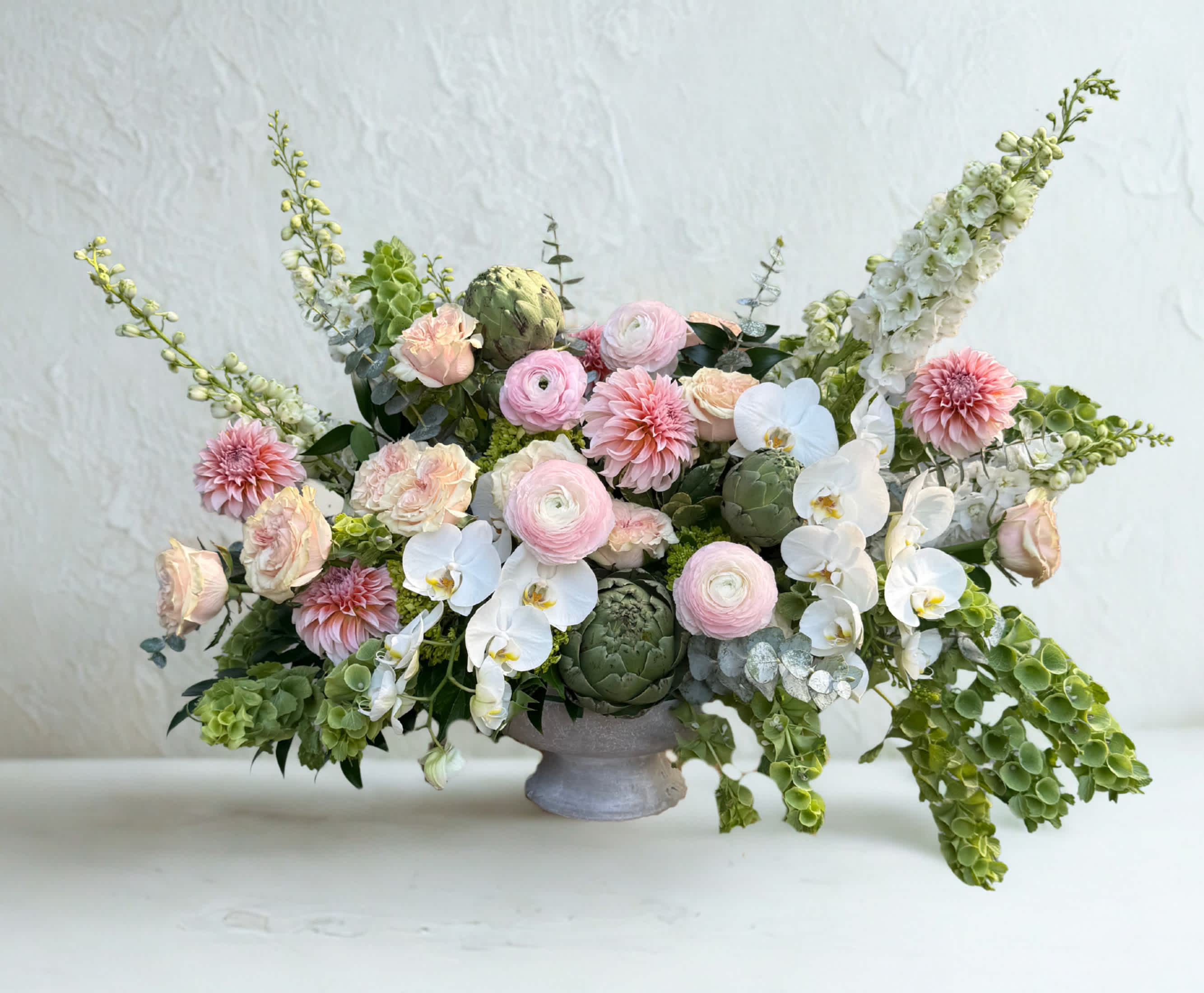 Low floral arrangement with pink blooms, white orchids, and green accents in a gray vase