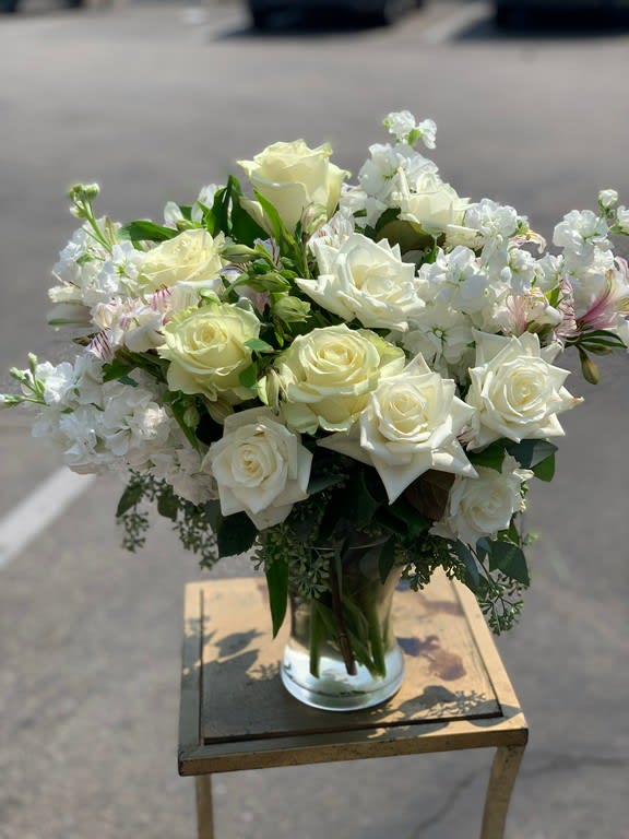 White roses and small white flowers arranged in a clear glass vase