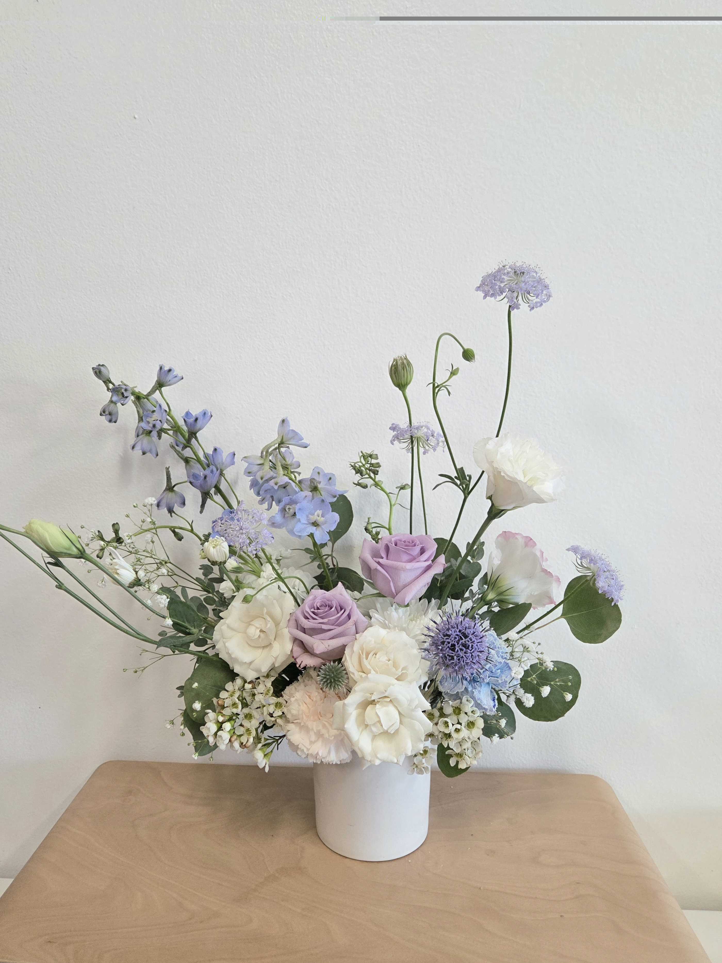 Pastel bouquet of lavender, white, and blue flowers in a white vase