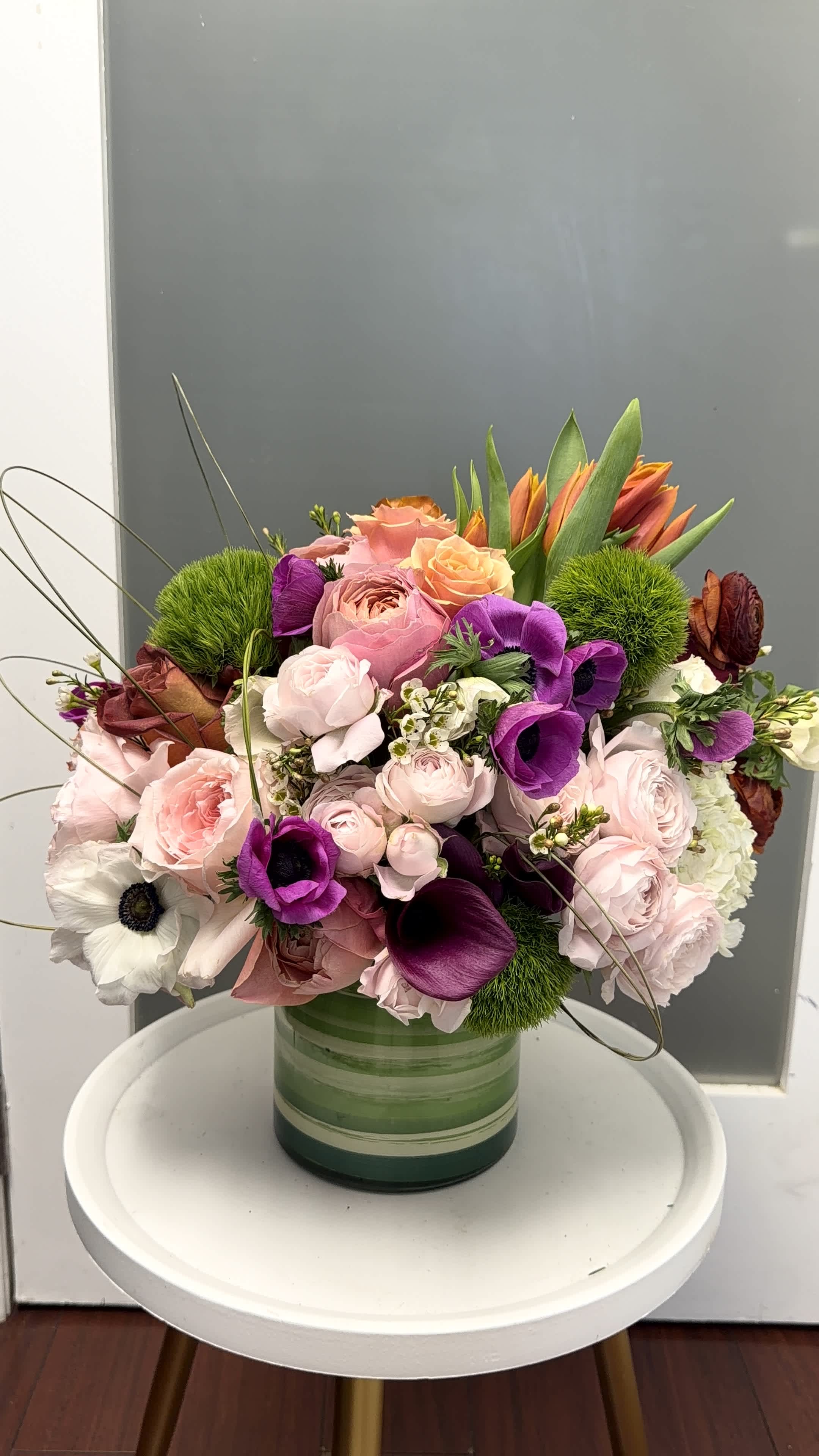 Mixed pink, purple, and orange flowers arranged in a green glass vase.