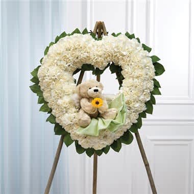 Heart-shaped white floral wreath with a teddy bear and ribbon on an easel