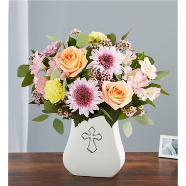 Mixed bouquet of roses and daisies in a white vase with a cross