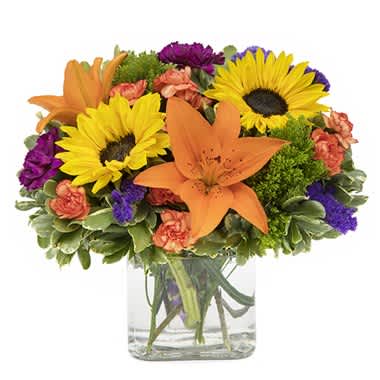 Bouquet of sunflowers, orange lilies, and purple flowers in a glass vase