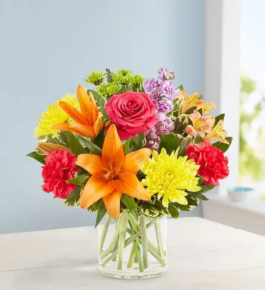 Mixed bouquet with orange lilies, pink rose, and yellow chrysanthemums in a glass vase