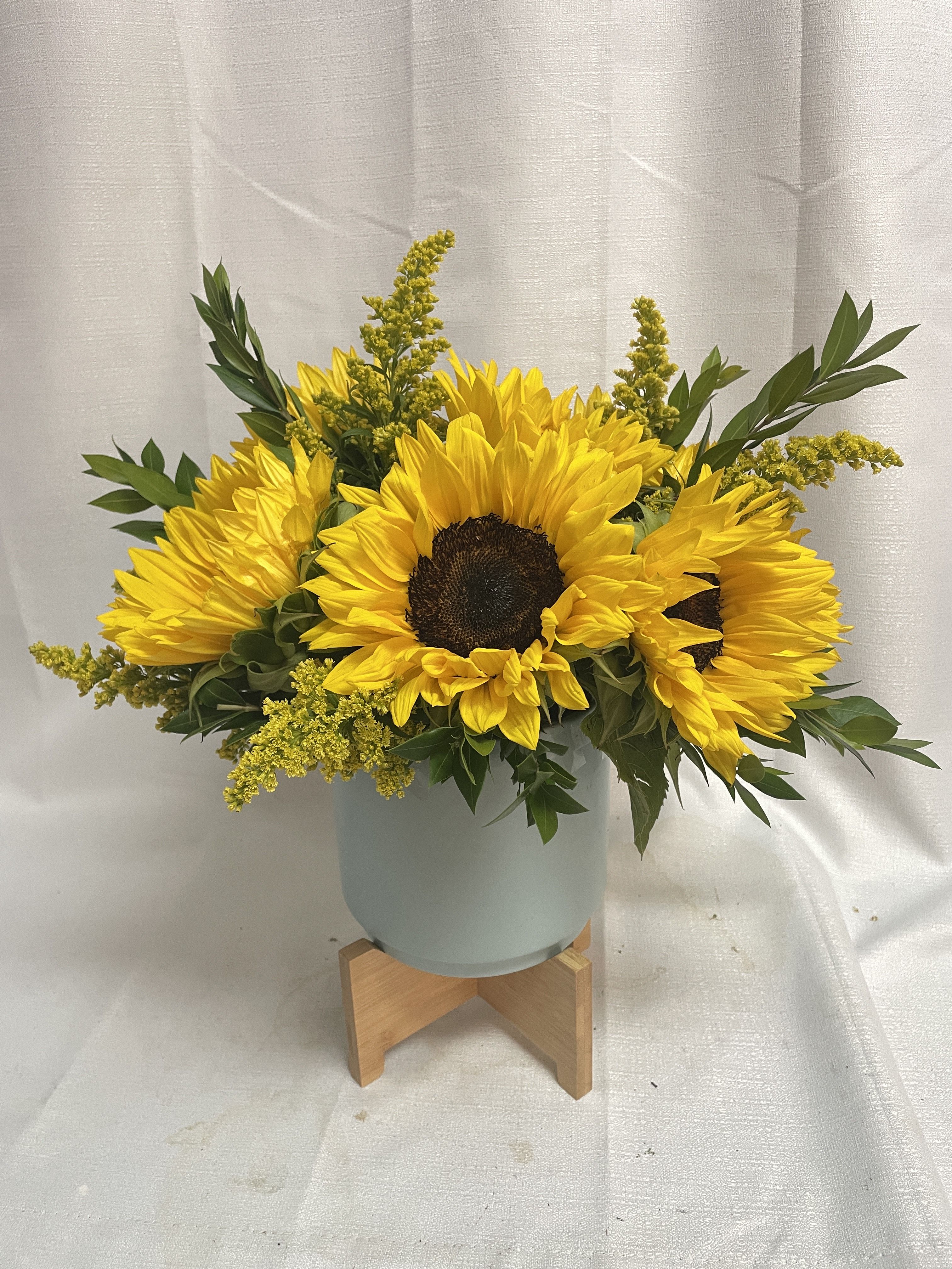 Sunflower arrangement in a pale blue vase on a wooden stand